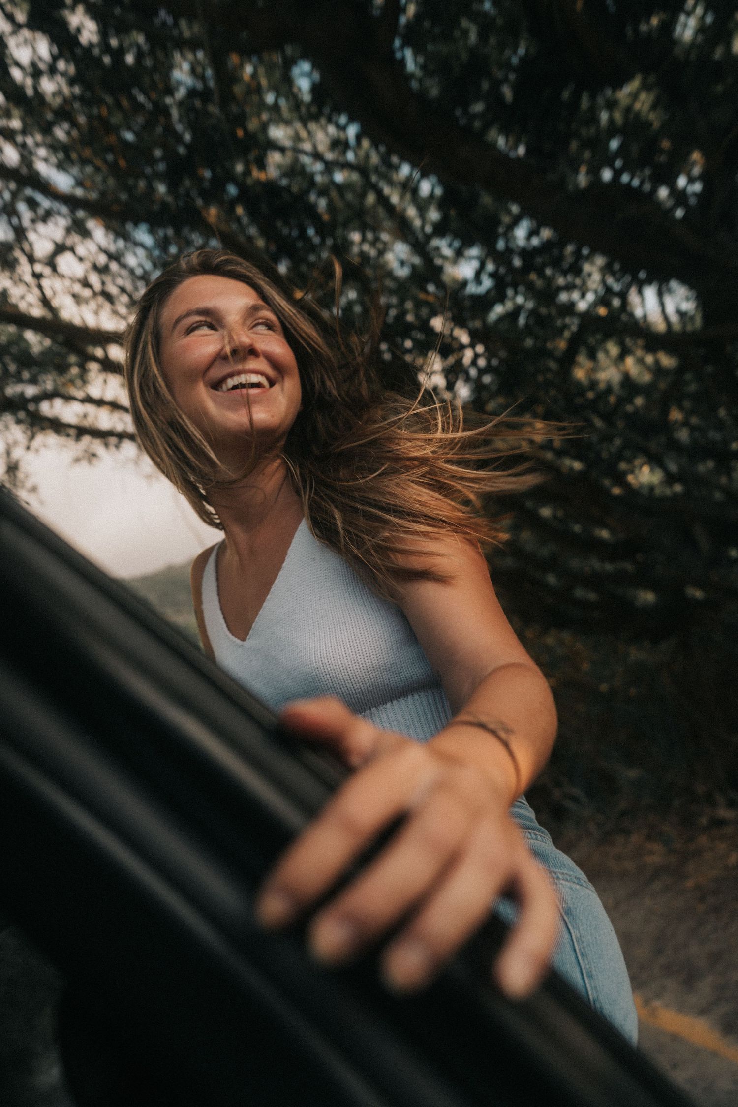 Person laughing joyfully while wind blows their hair during golden hour in a natural outdoor setting.