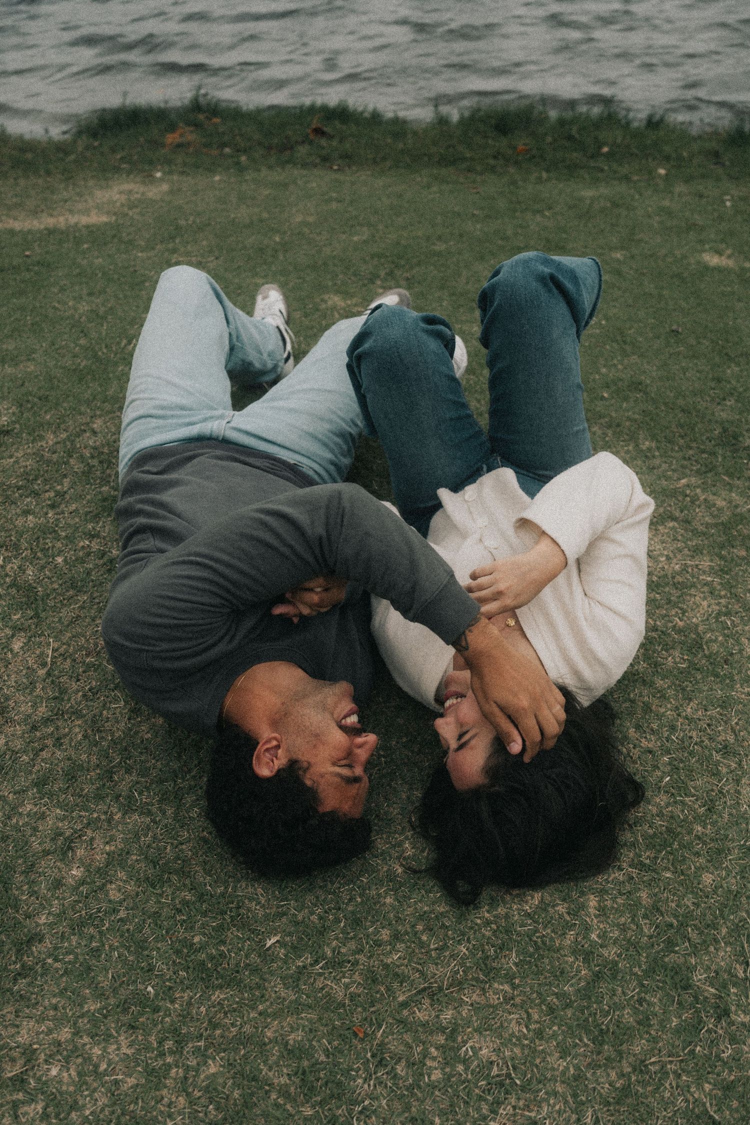 Two people lying close together on grass in coordinating grey and navy outfits.