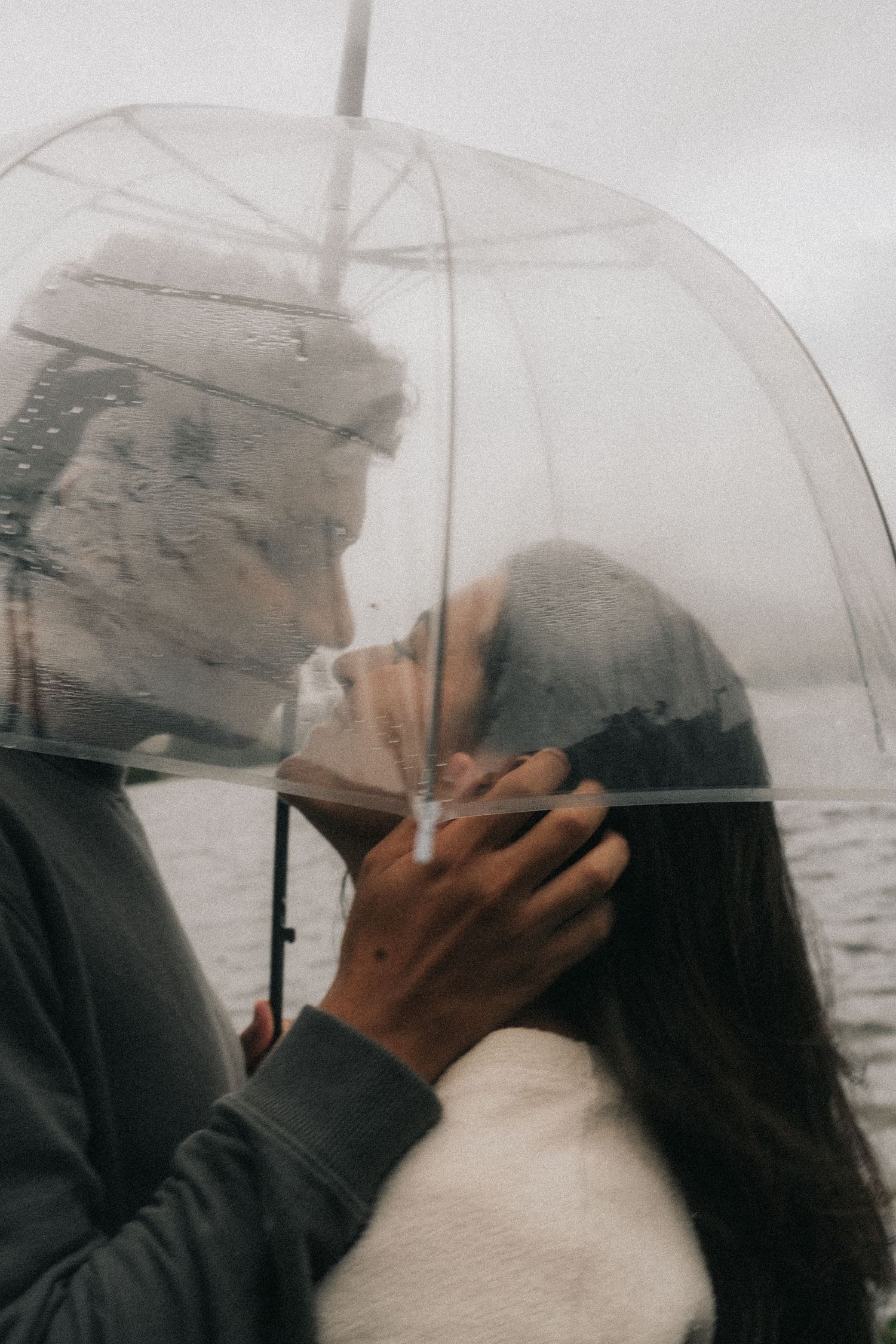 Romantic couple sharing intimate moment under clear umbrella on rainy day.