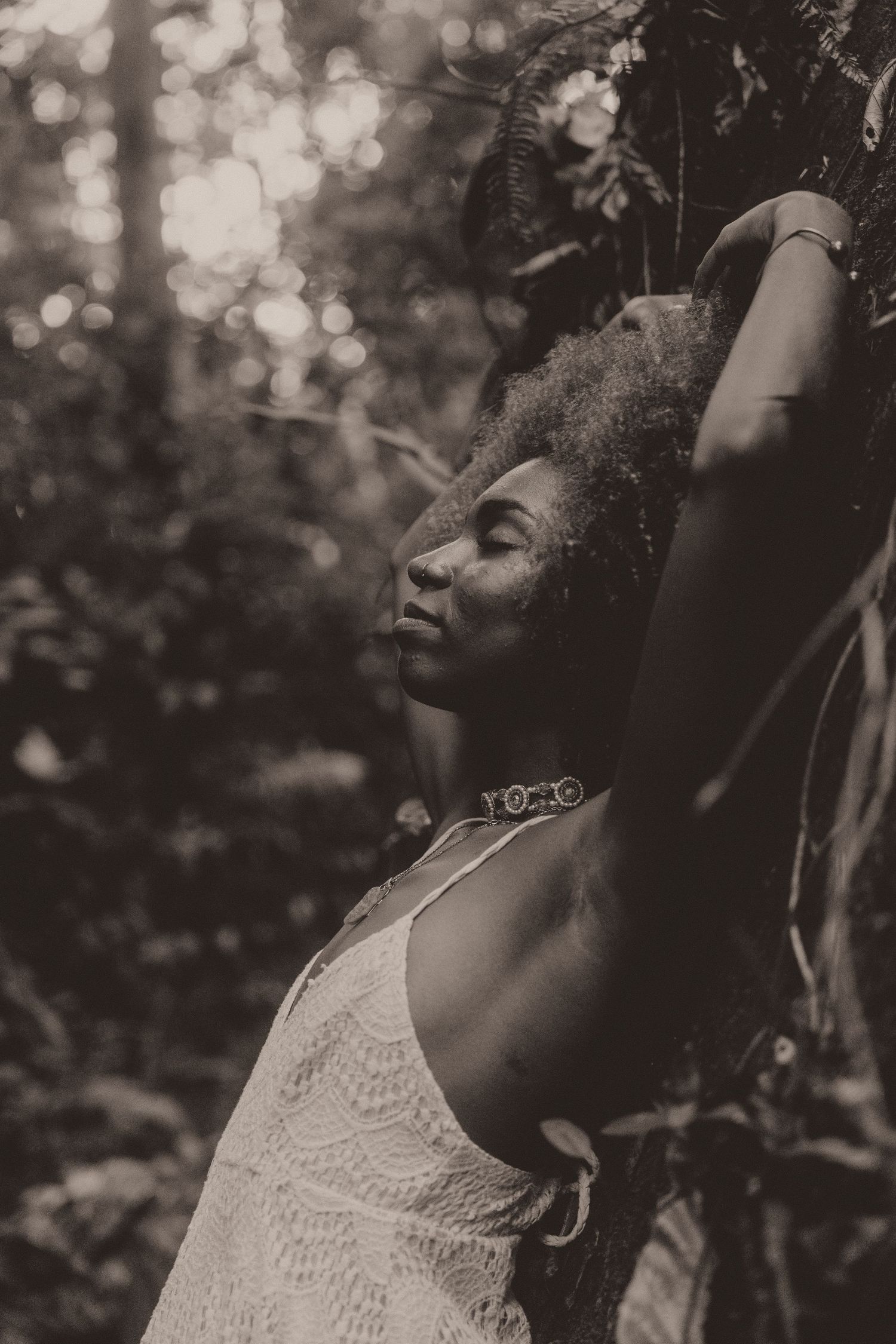 Black and white portrait series of a person in lace dress leaning against tree with eyes closed and soft natural lighting.