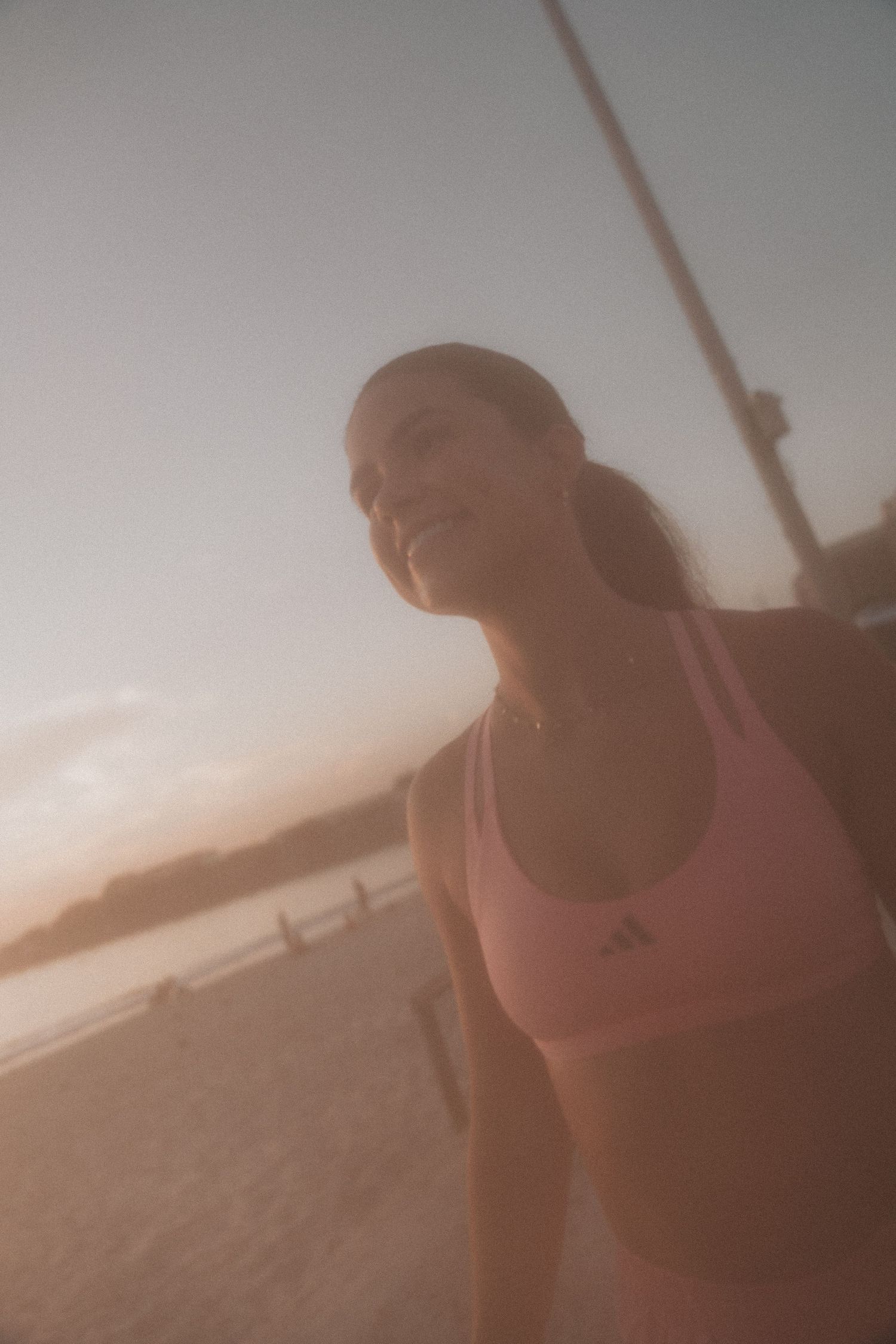 Athletic figure on a beach at sunset doing warmup stretches in pink activewear.