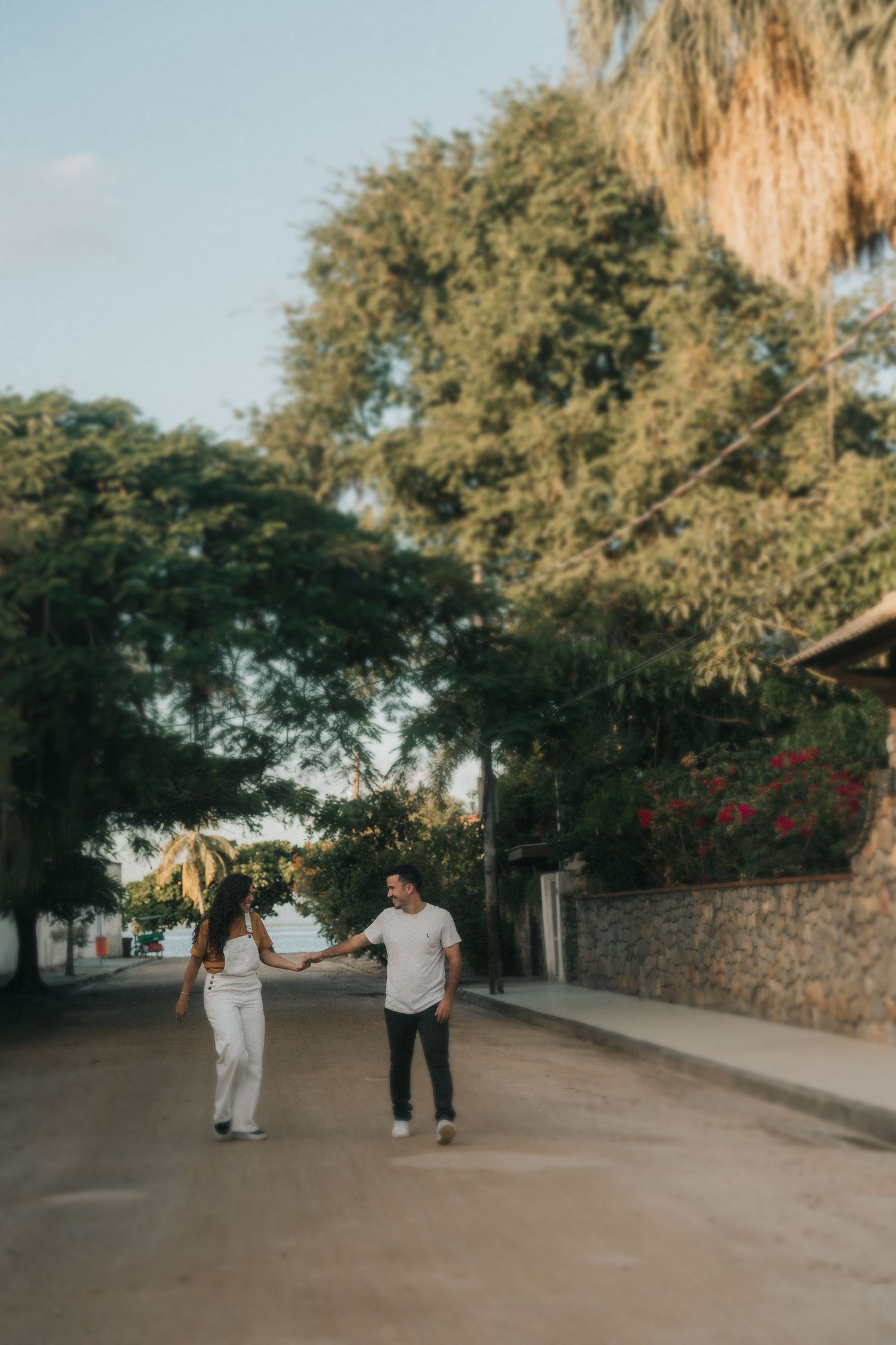A couple walks together down a shaded tree-lined path on a sunny afternoon.