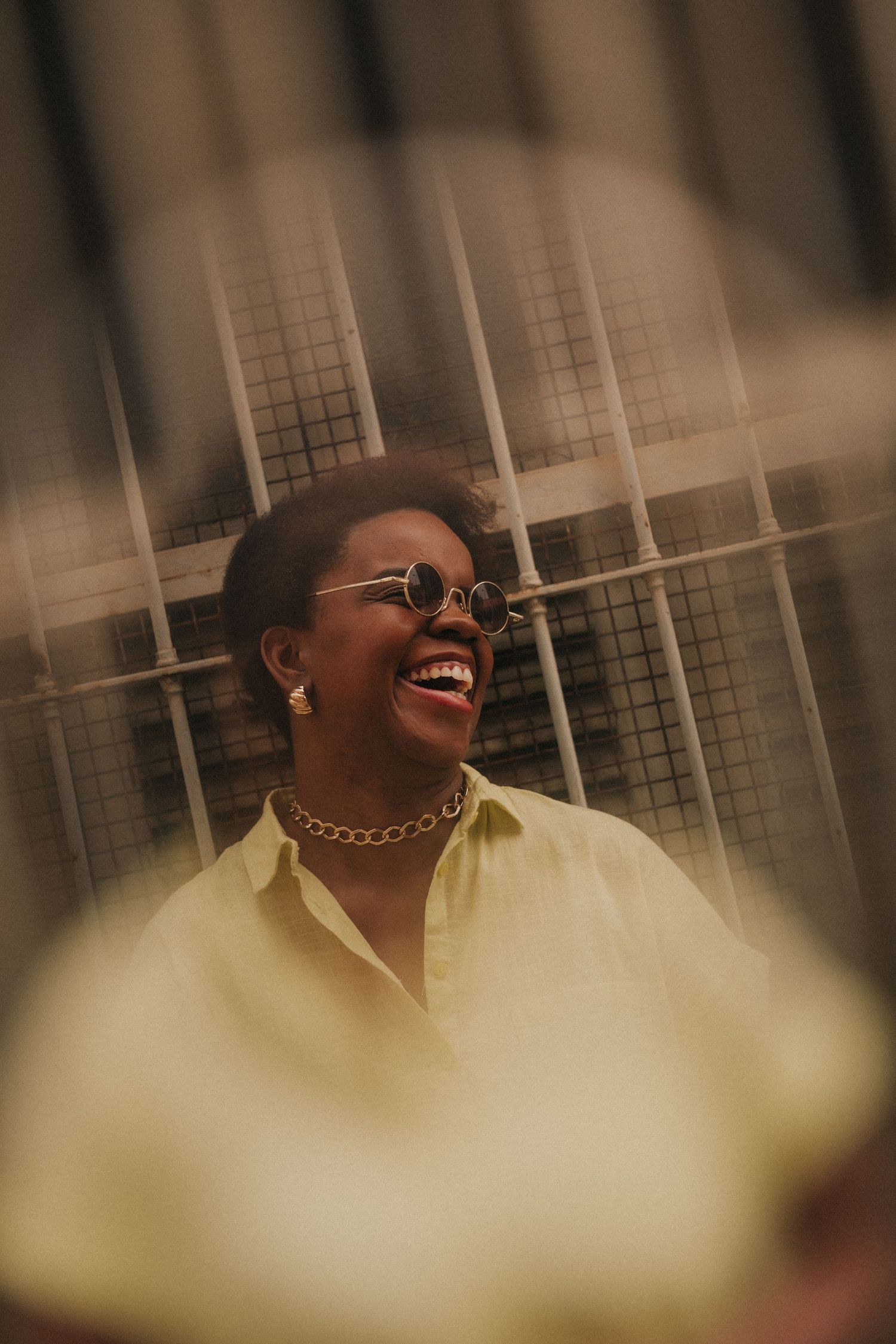 Person wearing glasses laughs joyfully while looking upward in a natural setting with blurred background.