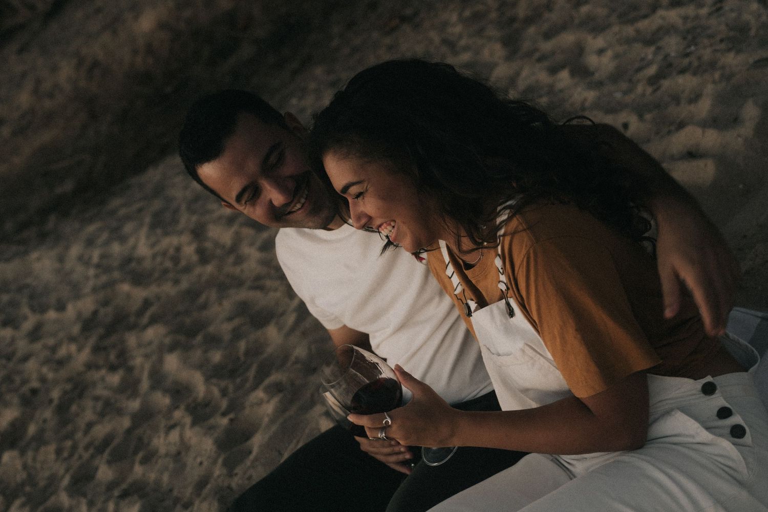 Couple shares an intimate moment while lying next to each other on a beach at sunset.