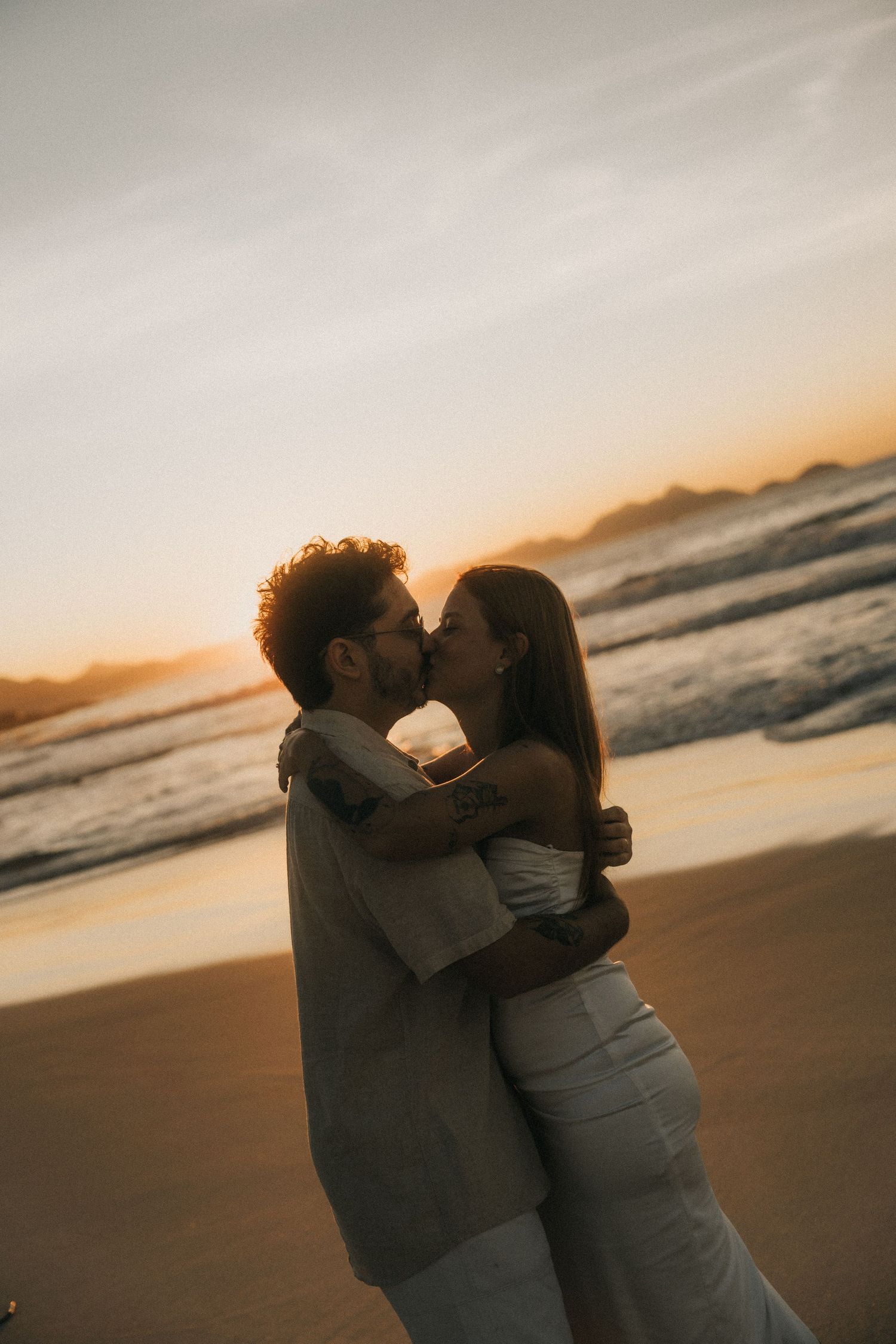 A romantic silhouette of a couple embracing on a beach at sunset as waves roll in along the shore.