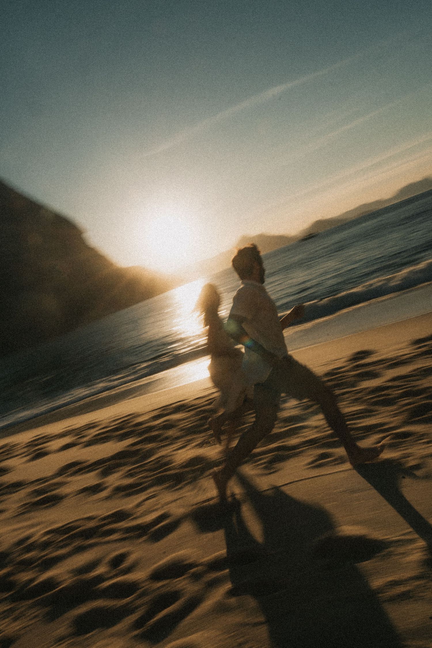 Silhouettes move along a beach at sunset with golden light reflecting off the ocean waves and sandy shoreline.