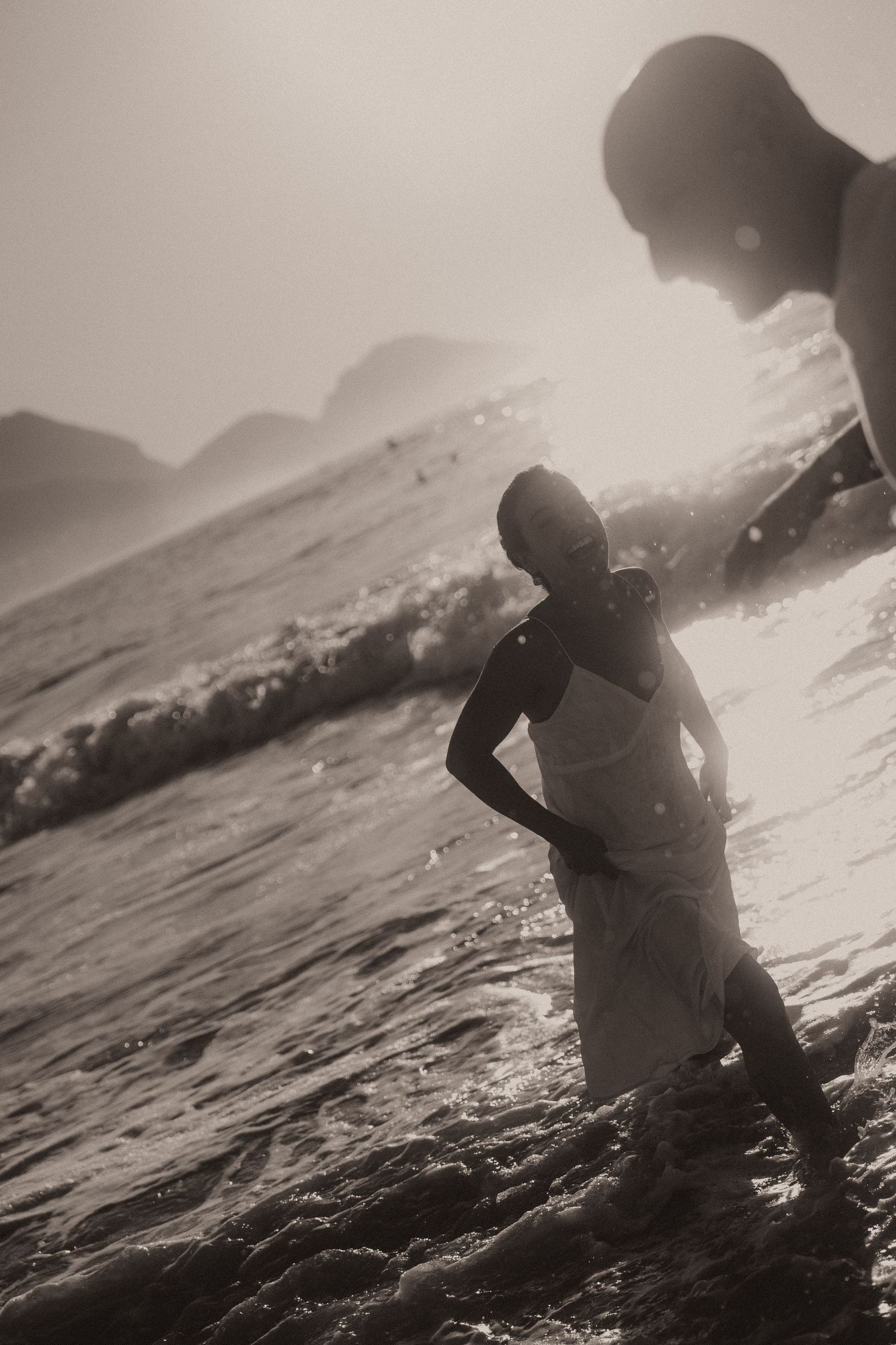 Silhouetted figures play in ocean waves at sunset, creating a dreamy sequence of motion captured in black and white.