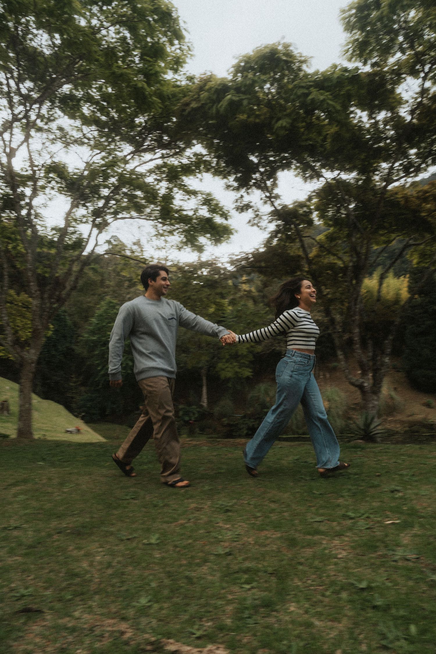 Four sequential photos show two people playfully falling backwards in slow motion on a grassy hillside.