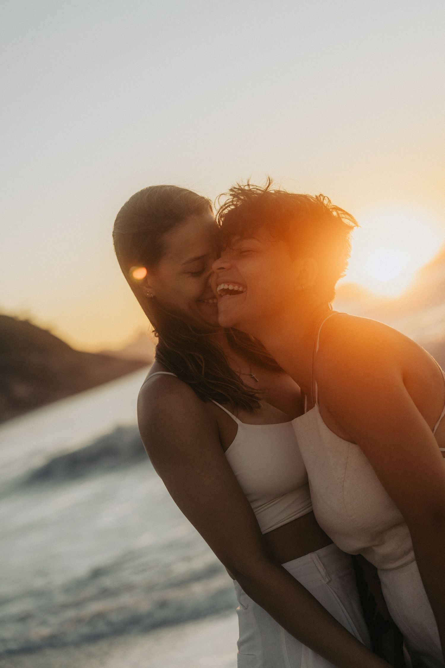 A romantic couple embraces on the beach at sunset with golden sunlight streaming through their silhouetted forms.