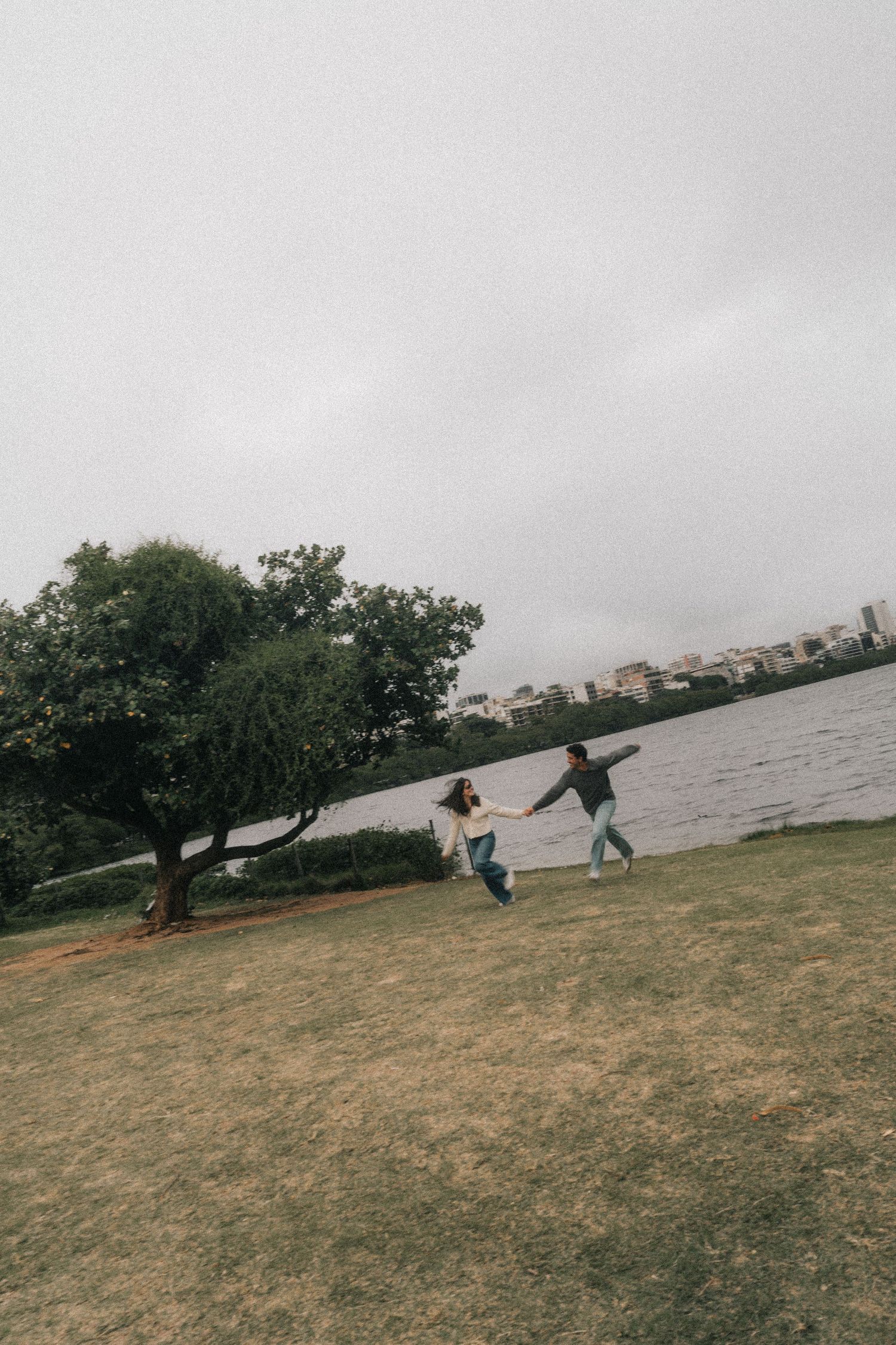 A sequence of five photos showing people leaning and walking against strong winds on a grassy hillside near a waterfront.