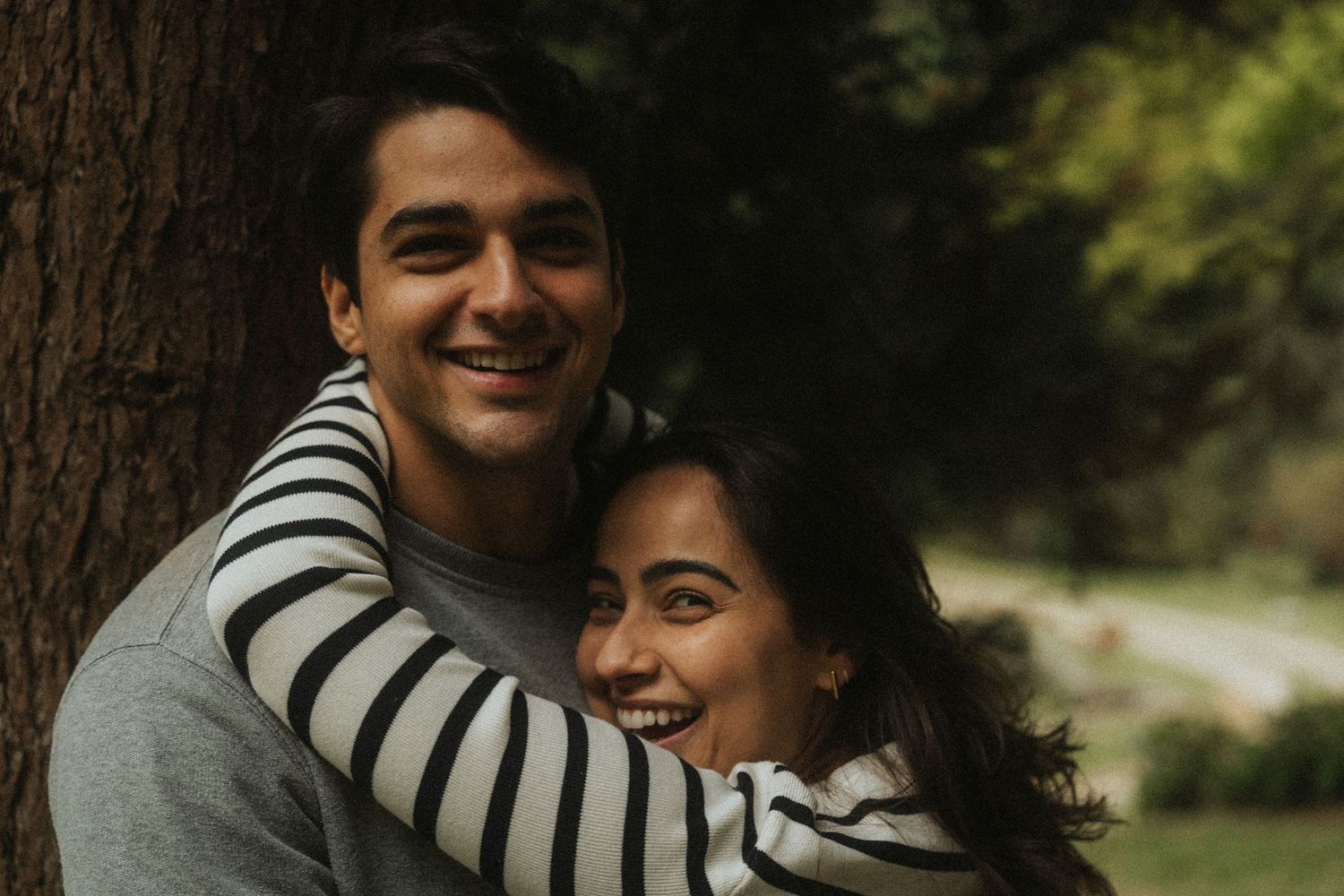Romantic couple in black and white striped clothing embrace and laugh together in a sunny outdoor setting.