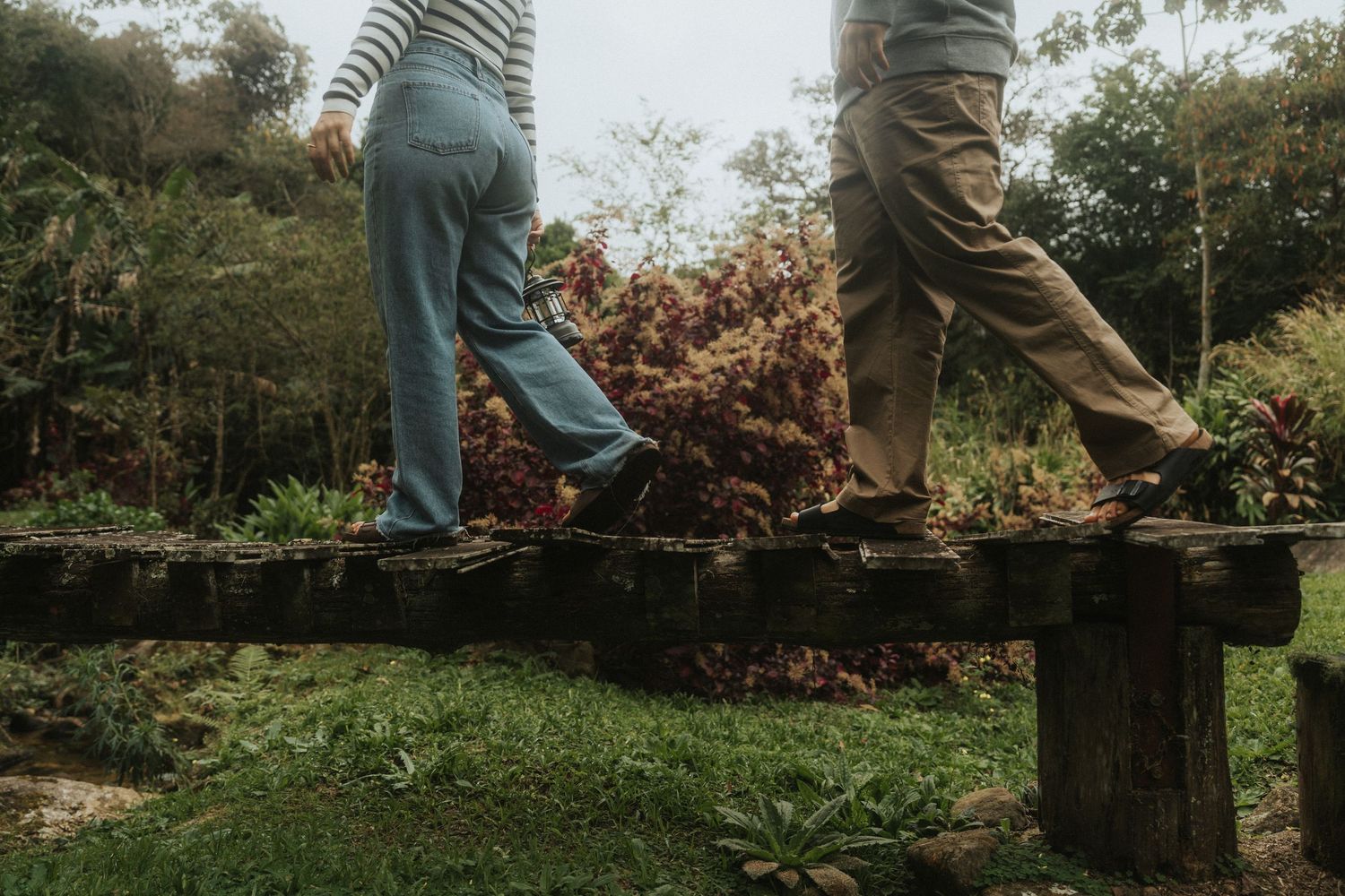 Two people in casual clothing stand on a wooden walkway surrounded by autumn foliage and greenery.