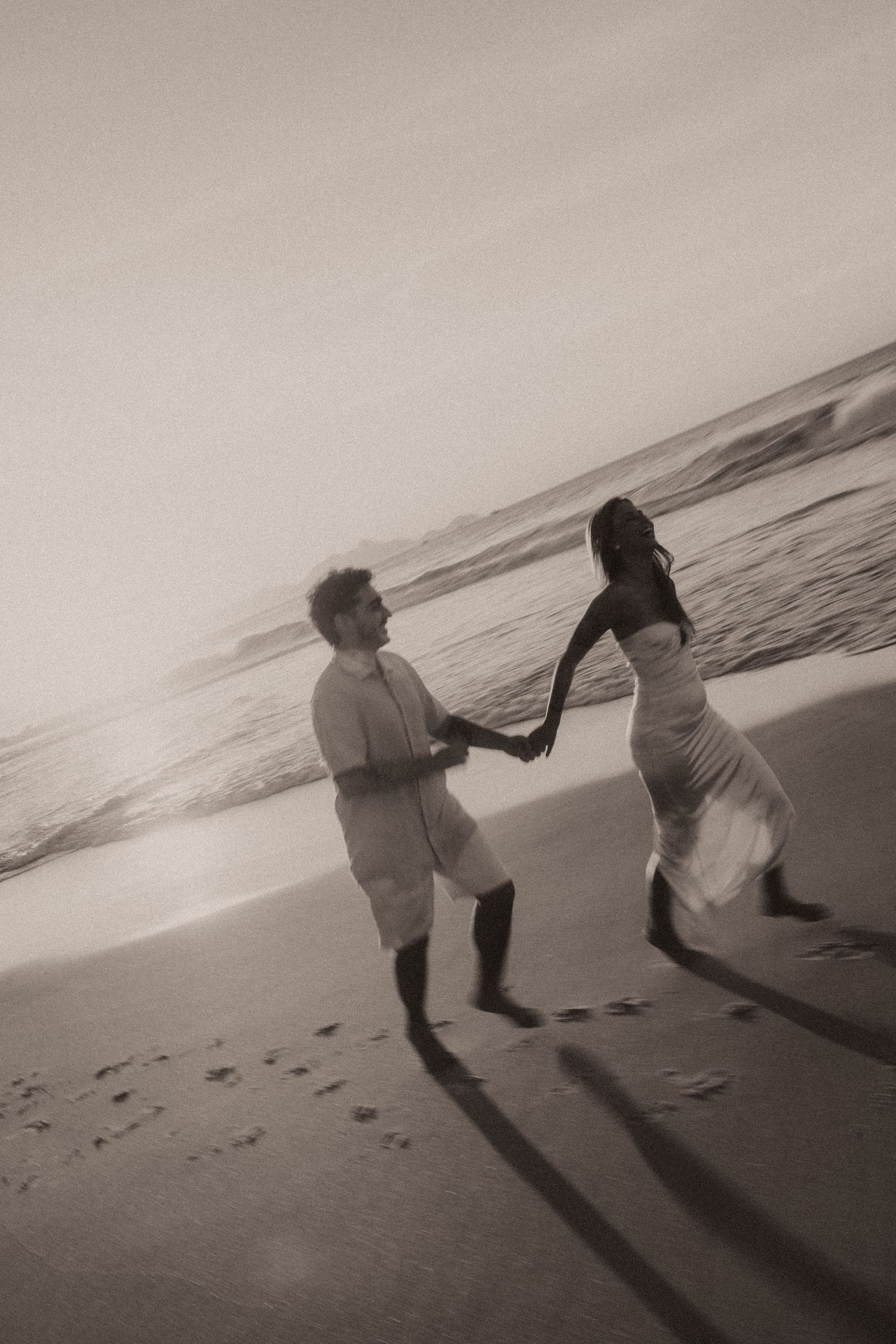 Two people casting long shadows on a beach at sunset as they play in the rolling waves of the ocean.