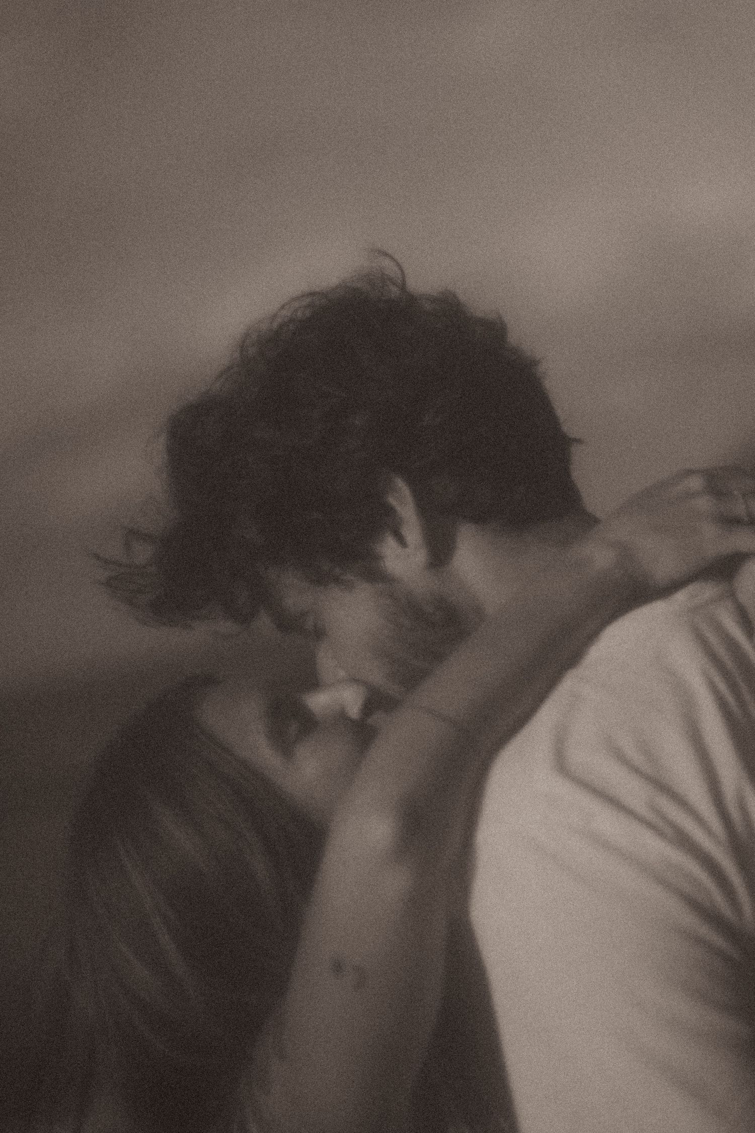 A set of connected grayscale photographs showing figures in an intimate embrace on a bed.