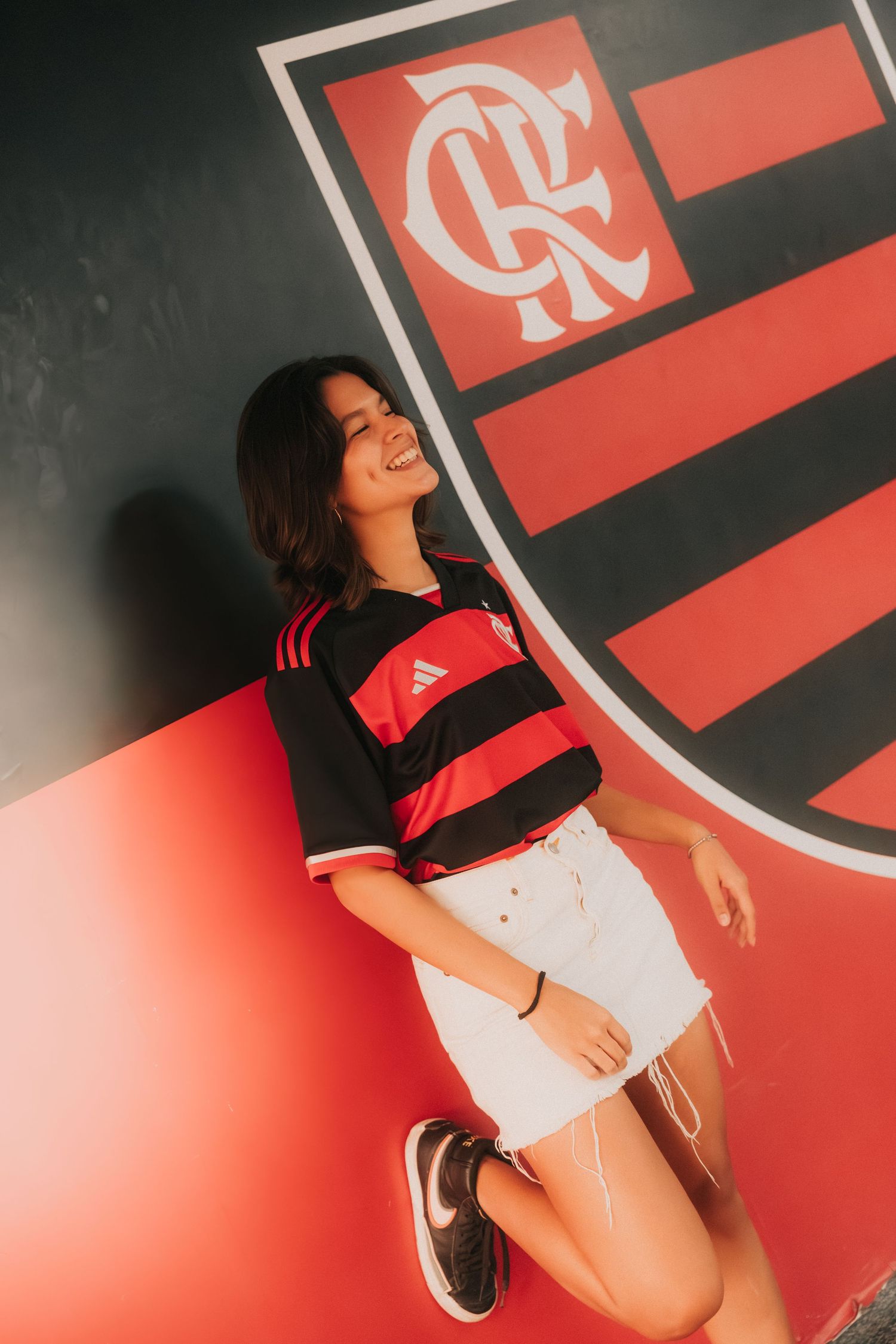 Fan poses wearing Flamengo soccer jersey against red and black striped club logo background.