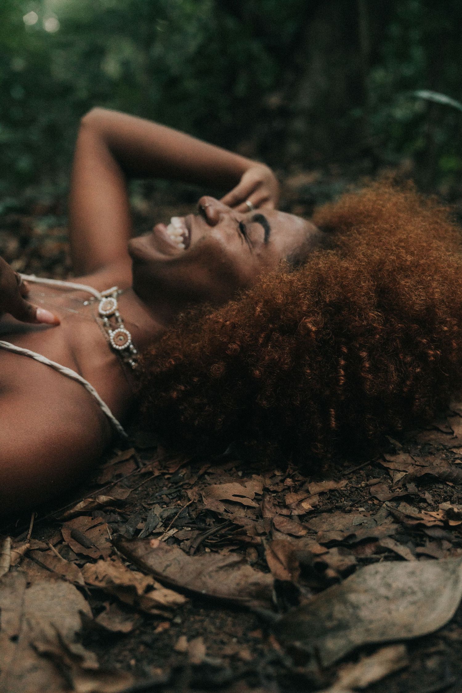 Artistic portrait of someone lying on autumn leaves with natural curly hair amidst a dreamy forest backdrop.