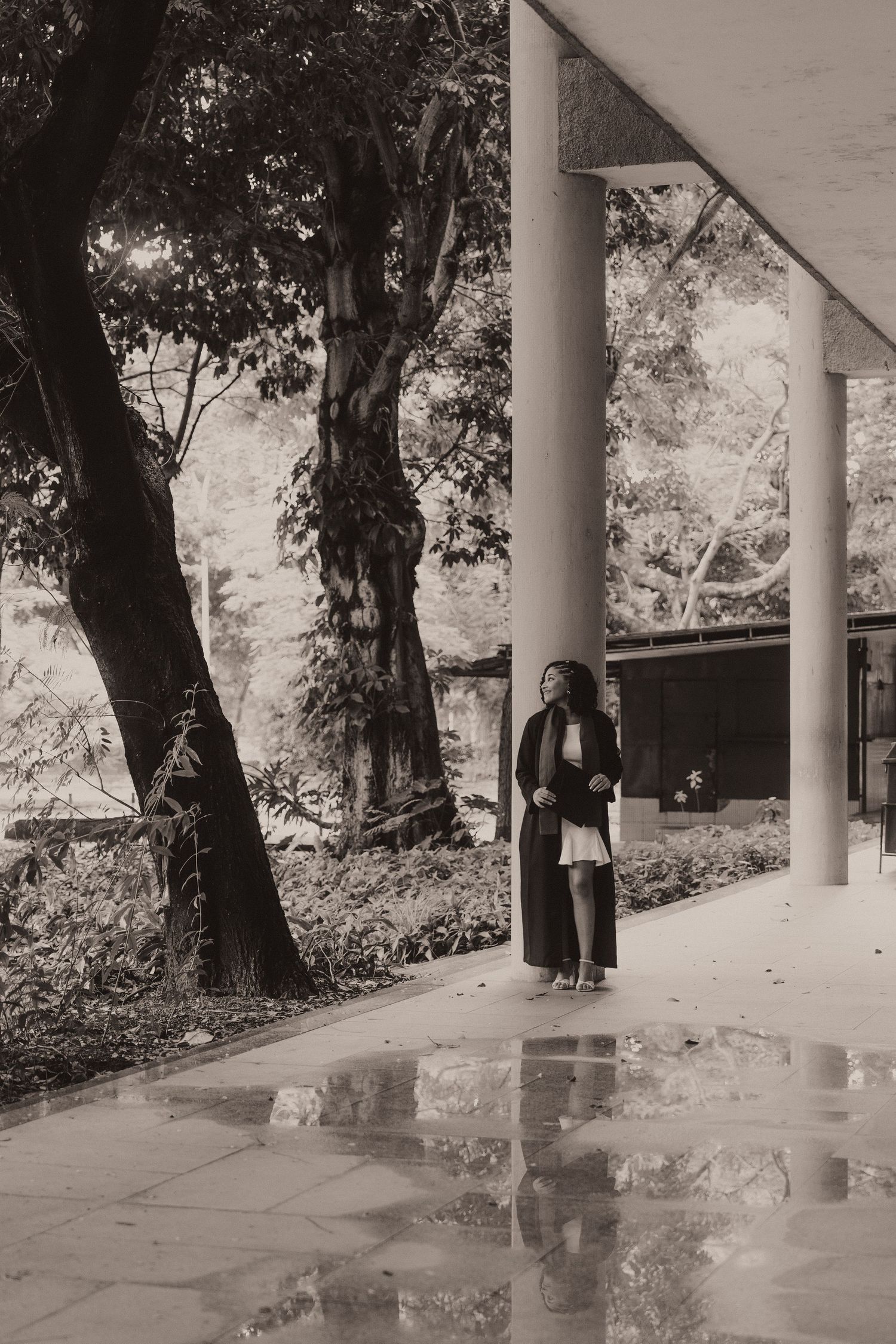 A sequence of black and white photos showing two figures walking along a covered colonnade walkway near trees.