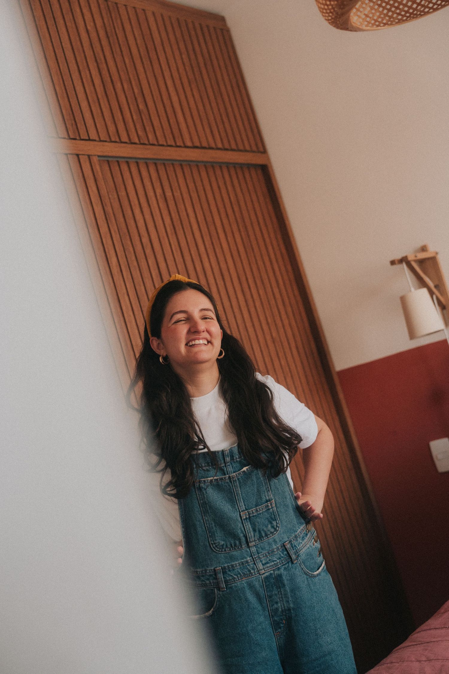 A series of candid photos showing someone in denim overalls smiling and laughing against a wooden wall and white background.