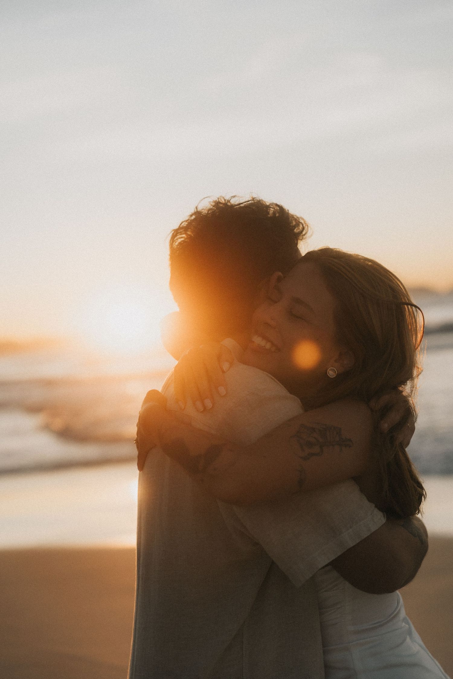 A couple embraces in a romantic kiss at sunset on the beach with golden sunlight streaming through the scene.