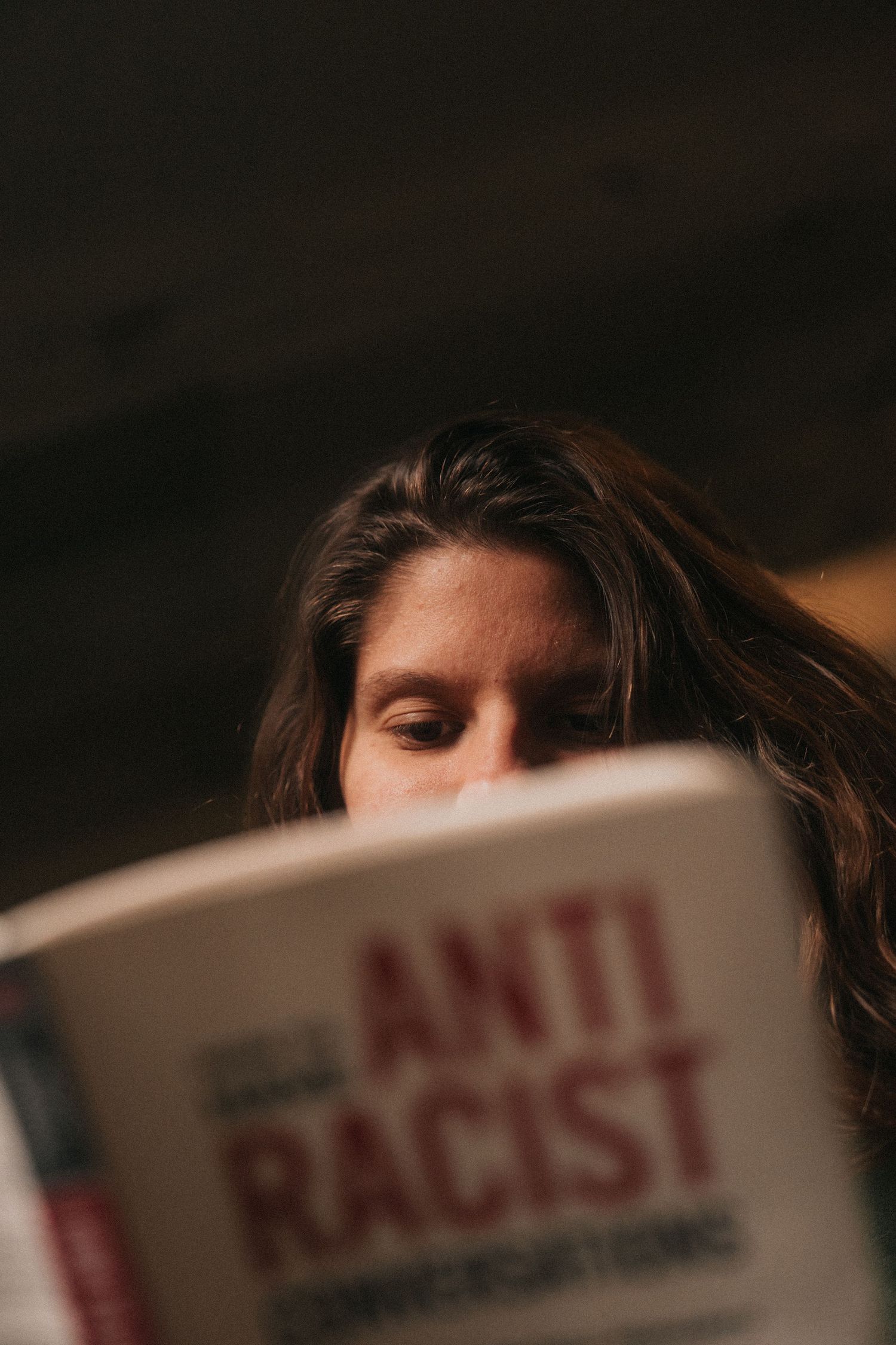 A close-up shot of someone reading a book titled 'Anti Racist' against a dark background.
