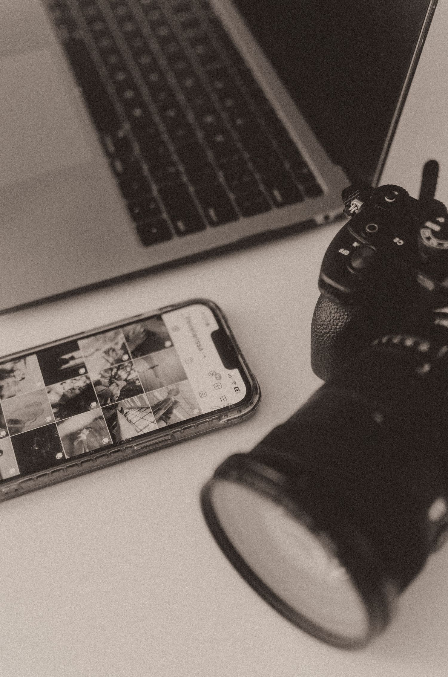 Laptop and smartphone setup on desk in moody black and white photography.