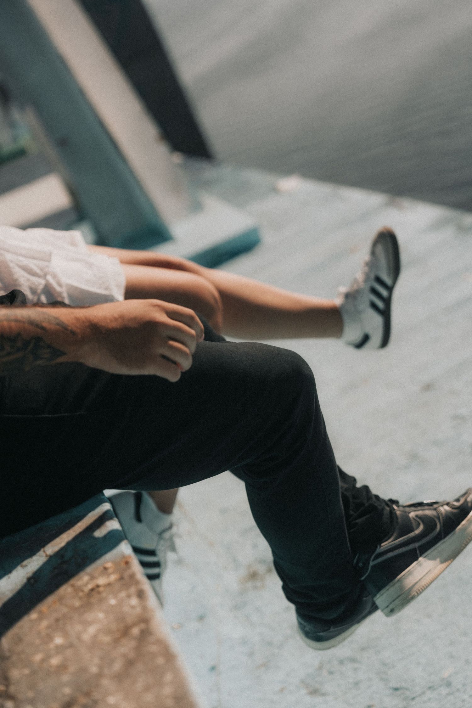 A person wearing dark jeans and sneakers sits casually on an edge with legs dangling in a moody atmospheric shot.
