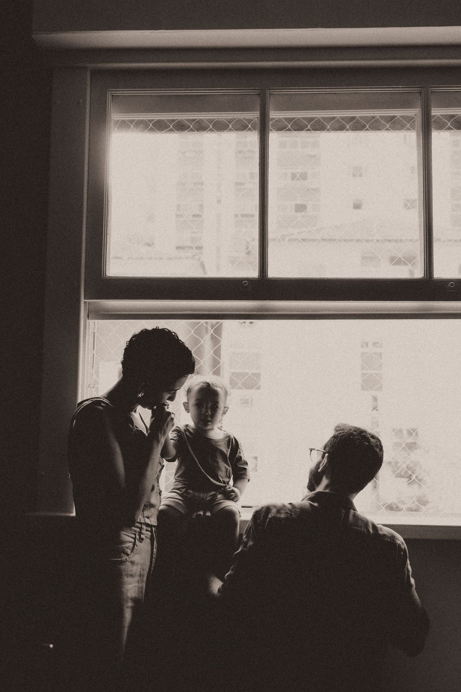A black and white silhouette of people by a window in moody lighting.