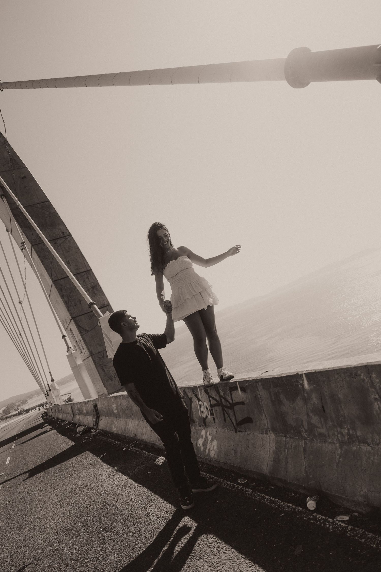 Black and white photo of two people on a large tilted structure, one reaching down to help the other against misty backdrop.