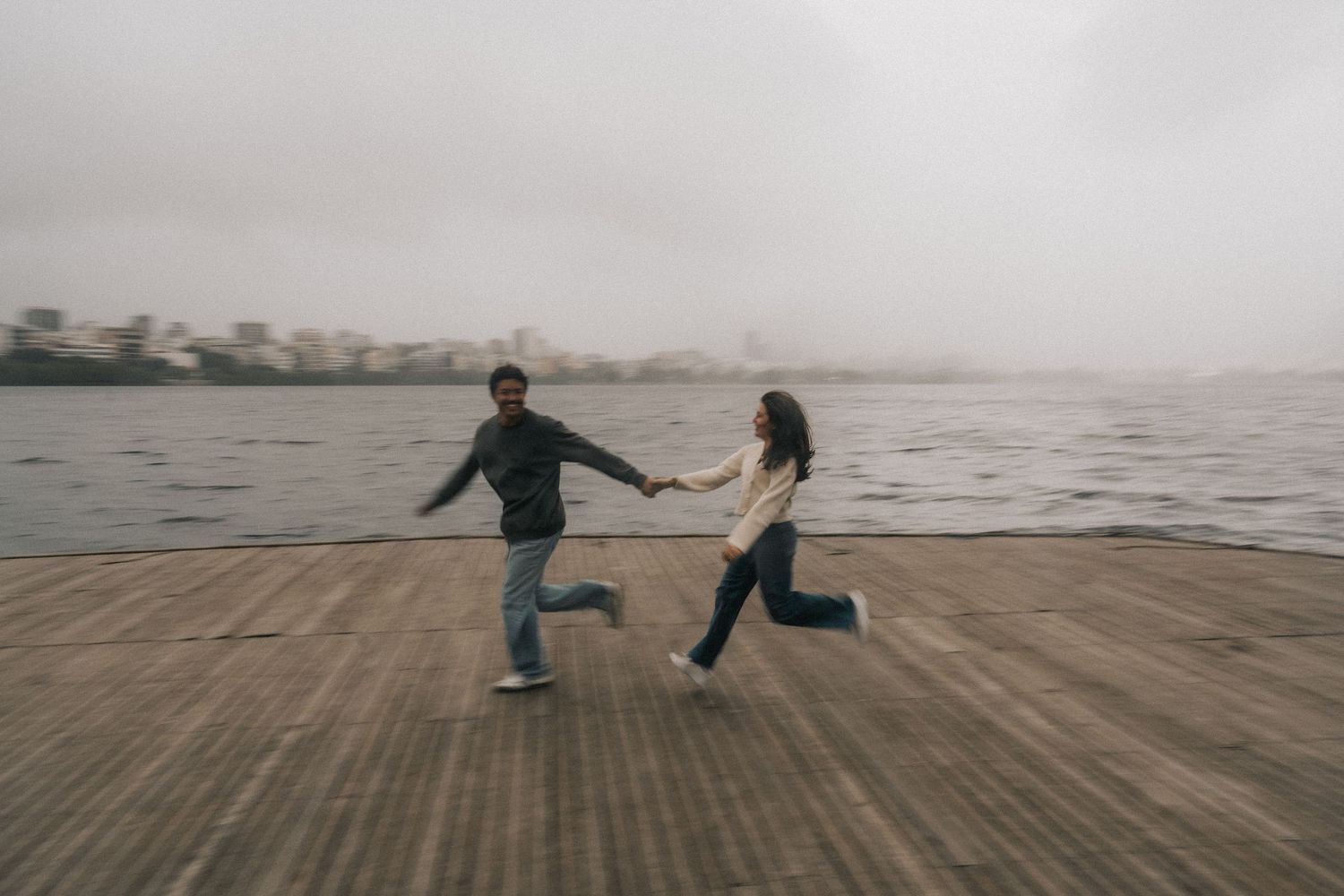 Distant figures walk along a misty beach boardwalk on an overcast day as fog rolls in from the ocean.