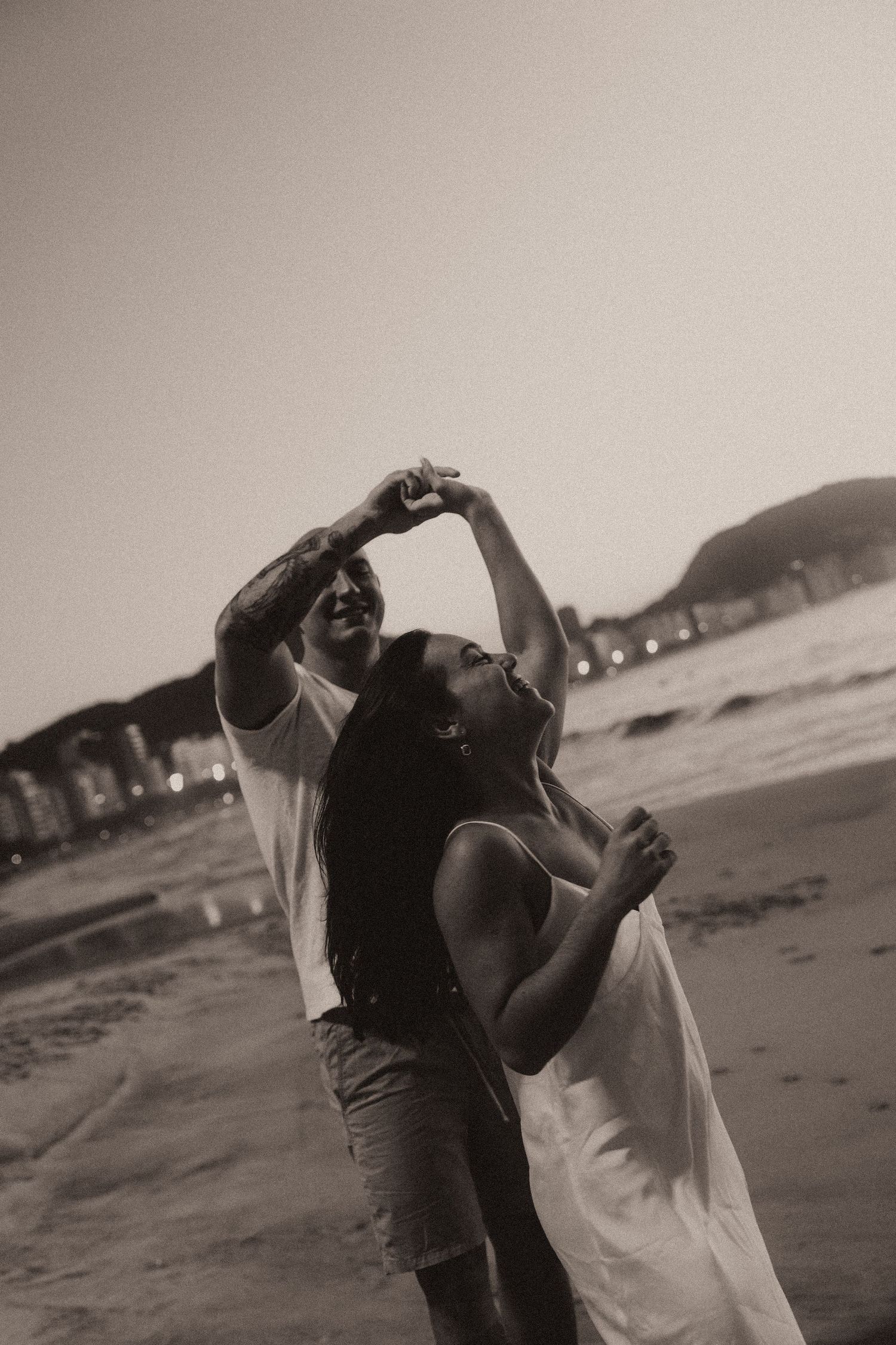Black and white panoramic sequence showing a romantic couple laughing and embracing on a beach at sunset.