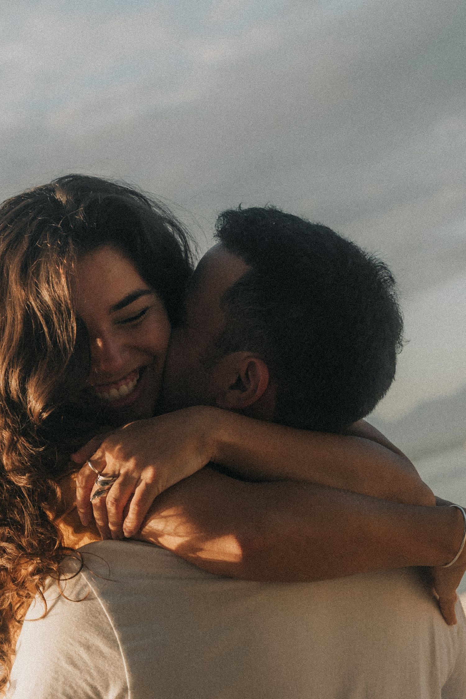 A tender moment between two people embracing at sunset, with warm backlighting creating a romantic silhouette.