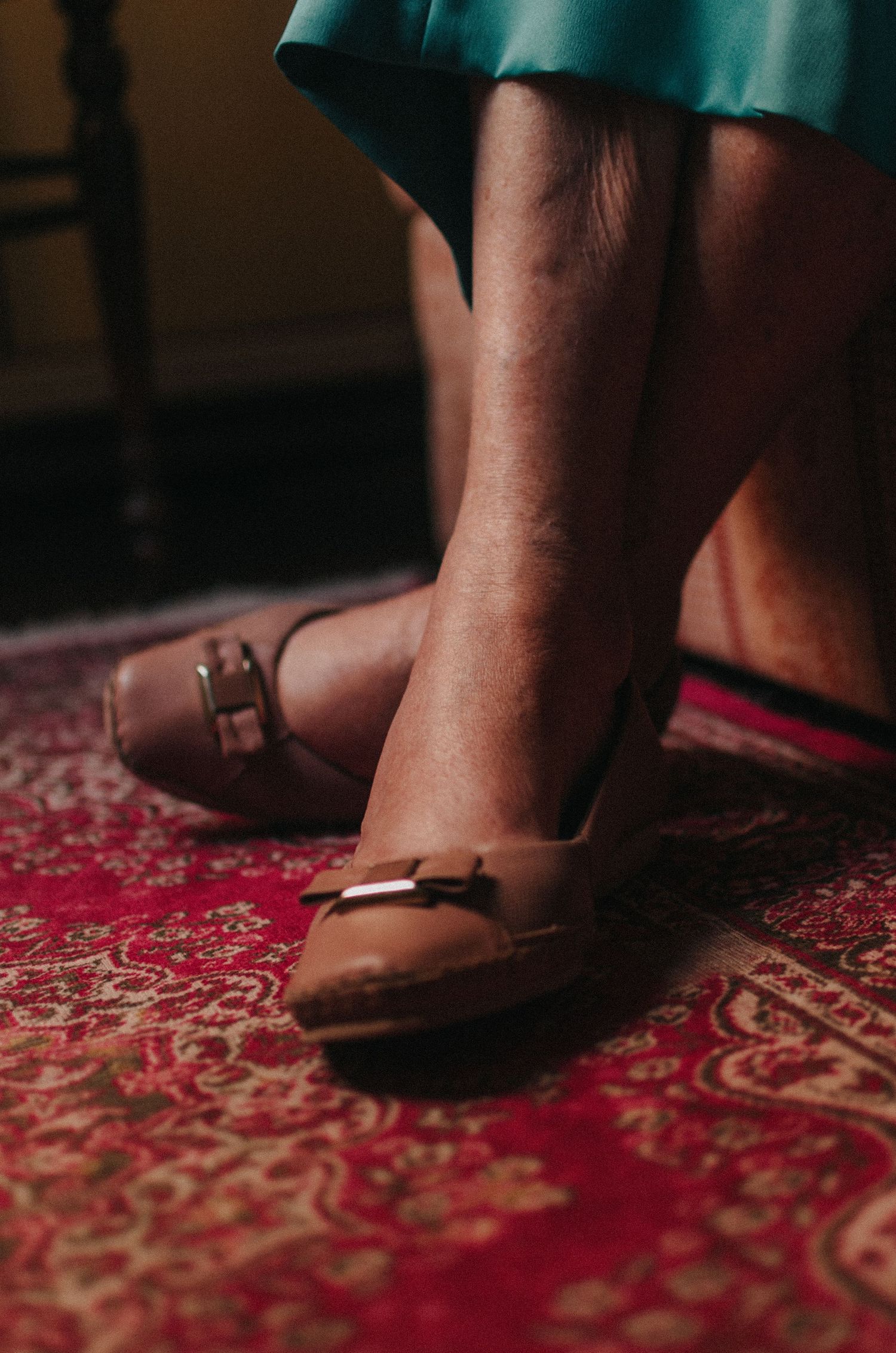 Feet in brown leather shoes stand on an ornate red and gold patterned carpet.
