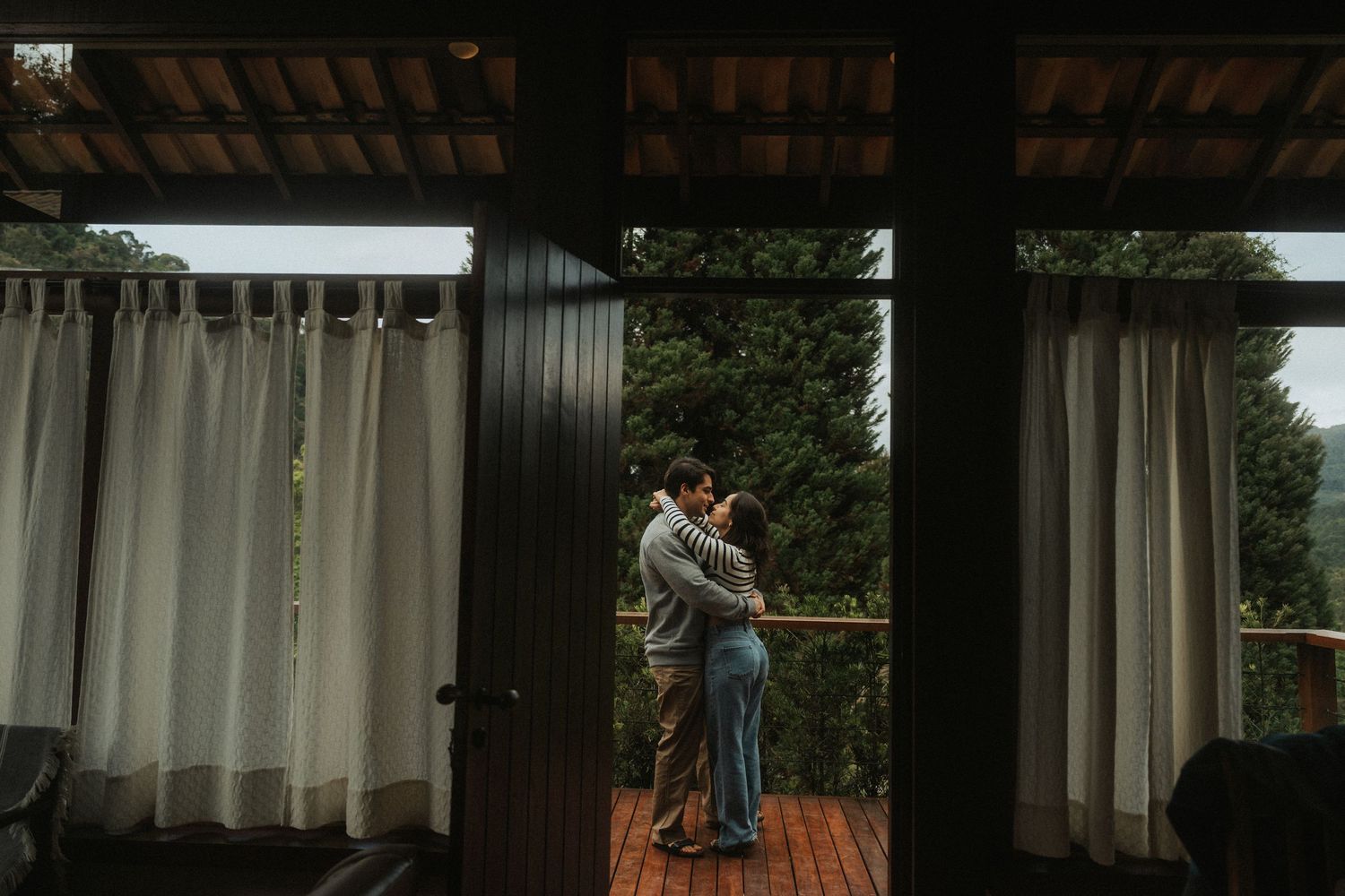 A couple dances together on a wooden deck surrounded by white curtains and greenery in the background.