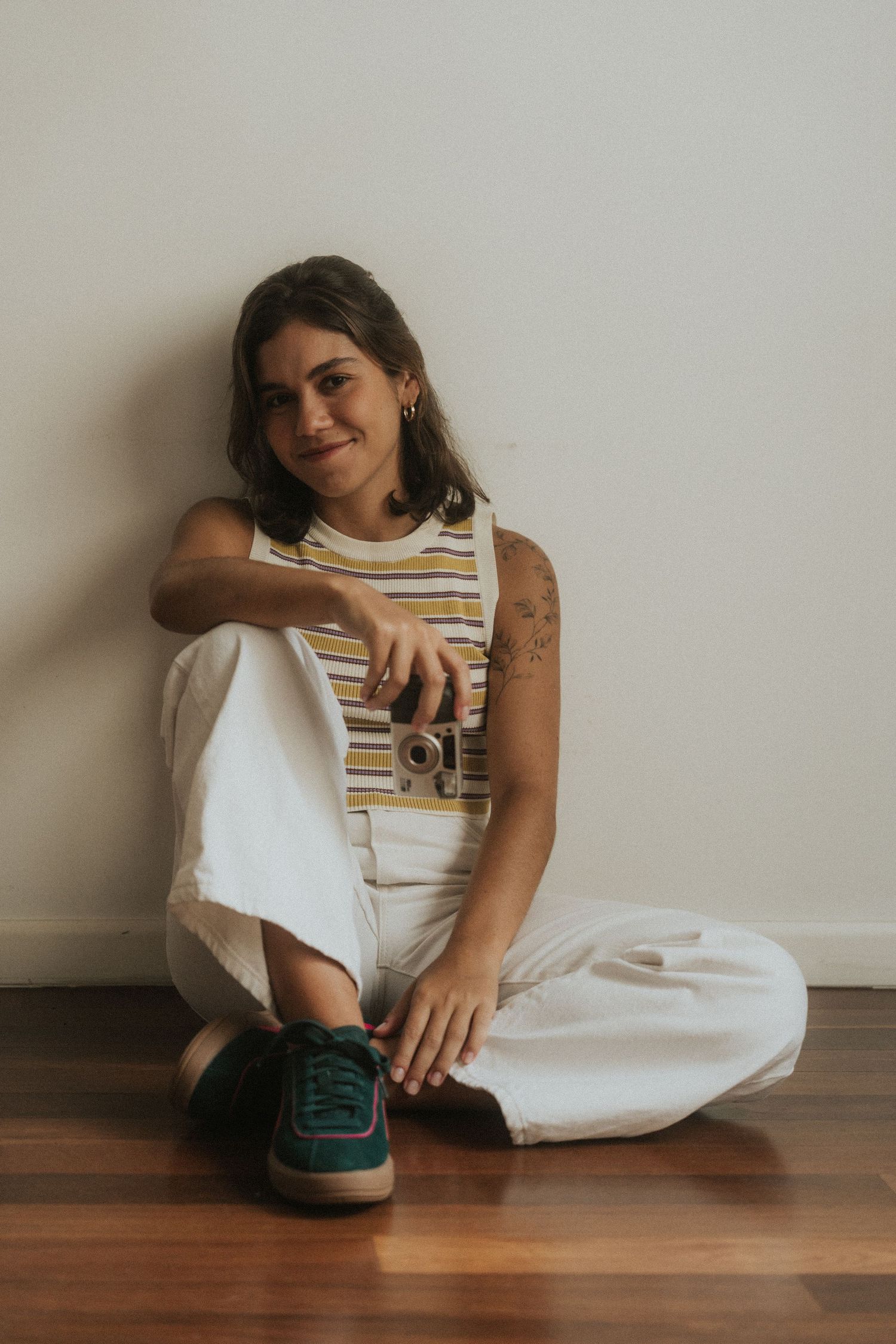 A person in a white dress sits casually on hardwood flooring against a beige wall in a series of candid poses.