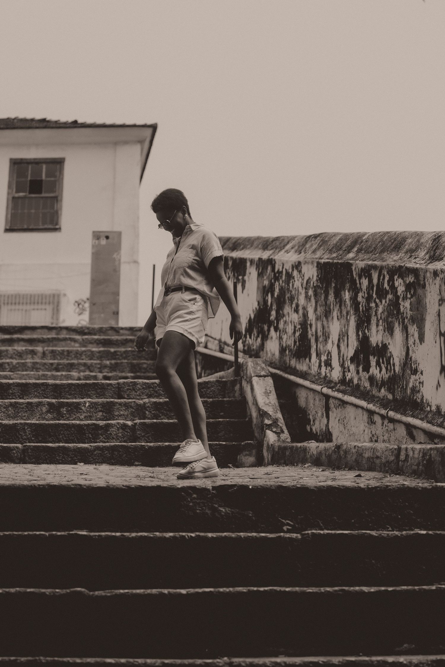 A person in casual attire descends a concrete staircase against a weathered wall in a black and white photograph.