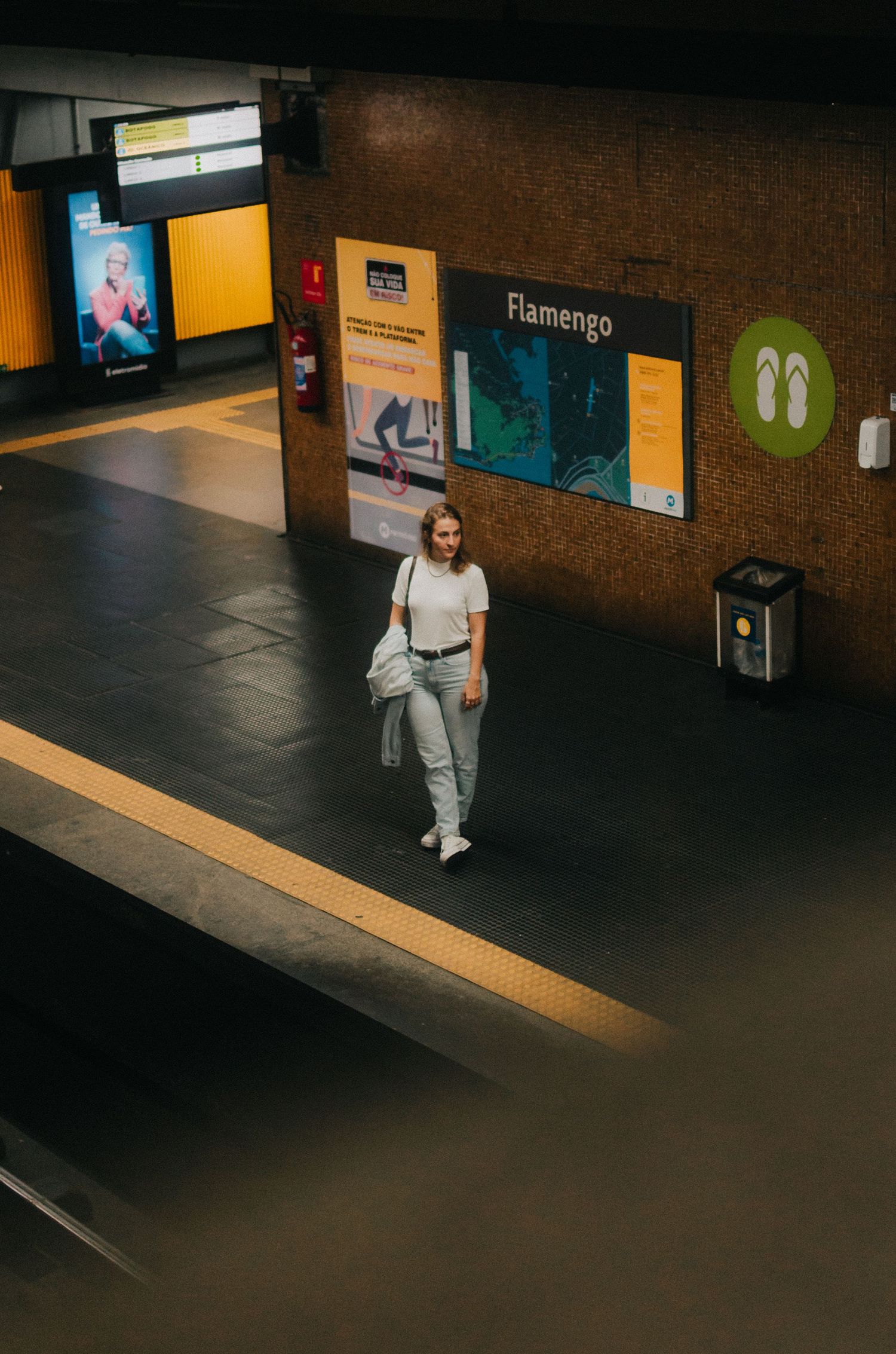 A person in light colored clothing sits on a yellow tiled bench in a dimly lit metro station.