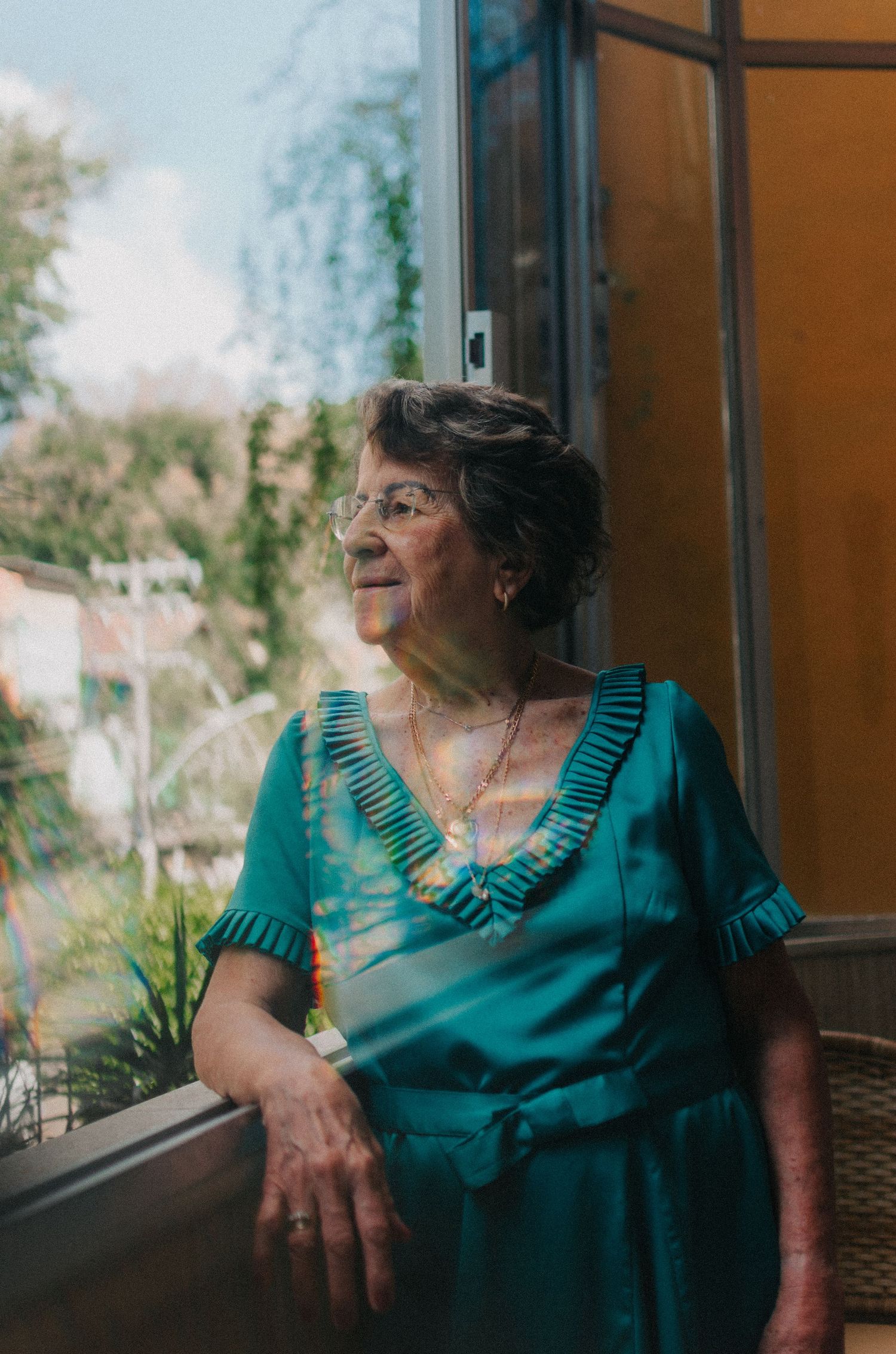 Person in a turquoise dress sits by a window while gazing thoughtfully outside in contemplative repose.