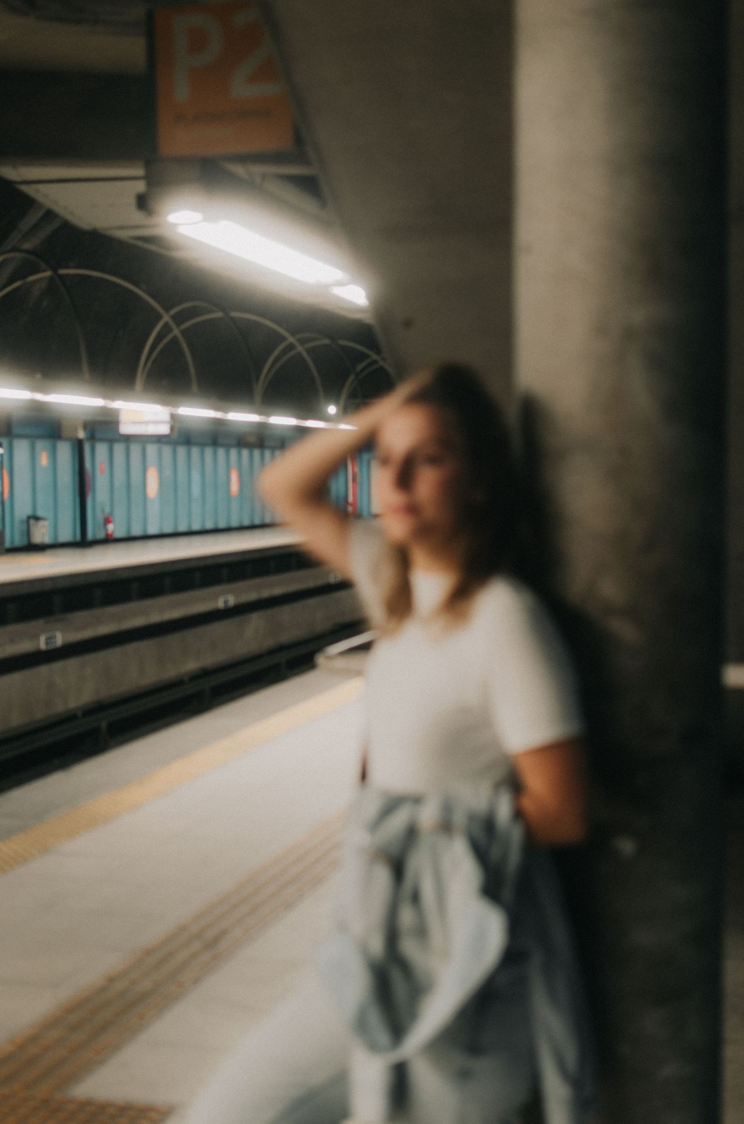 A moody subway station scene with fluorescent lighting and blurred figure waiting on the platform.