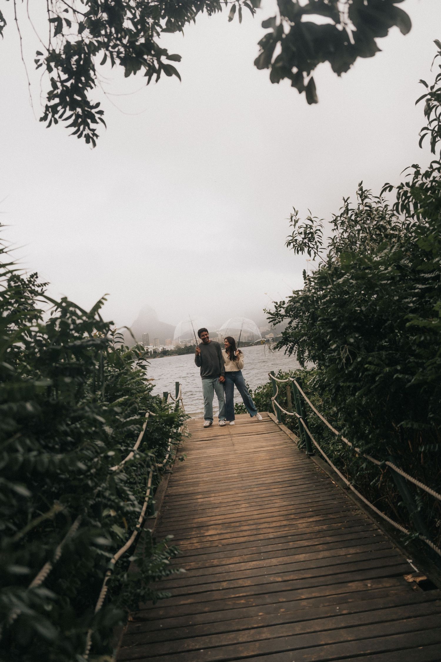 People walking along a foggy wooden boardwalk surrounded by lush foliage on a misty morning.