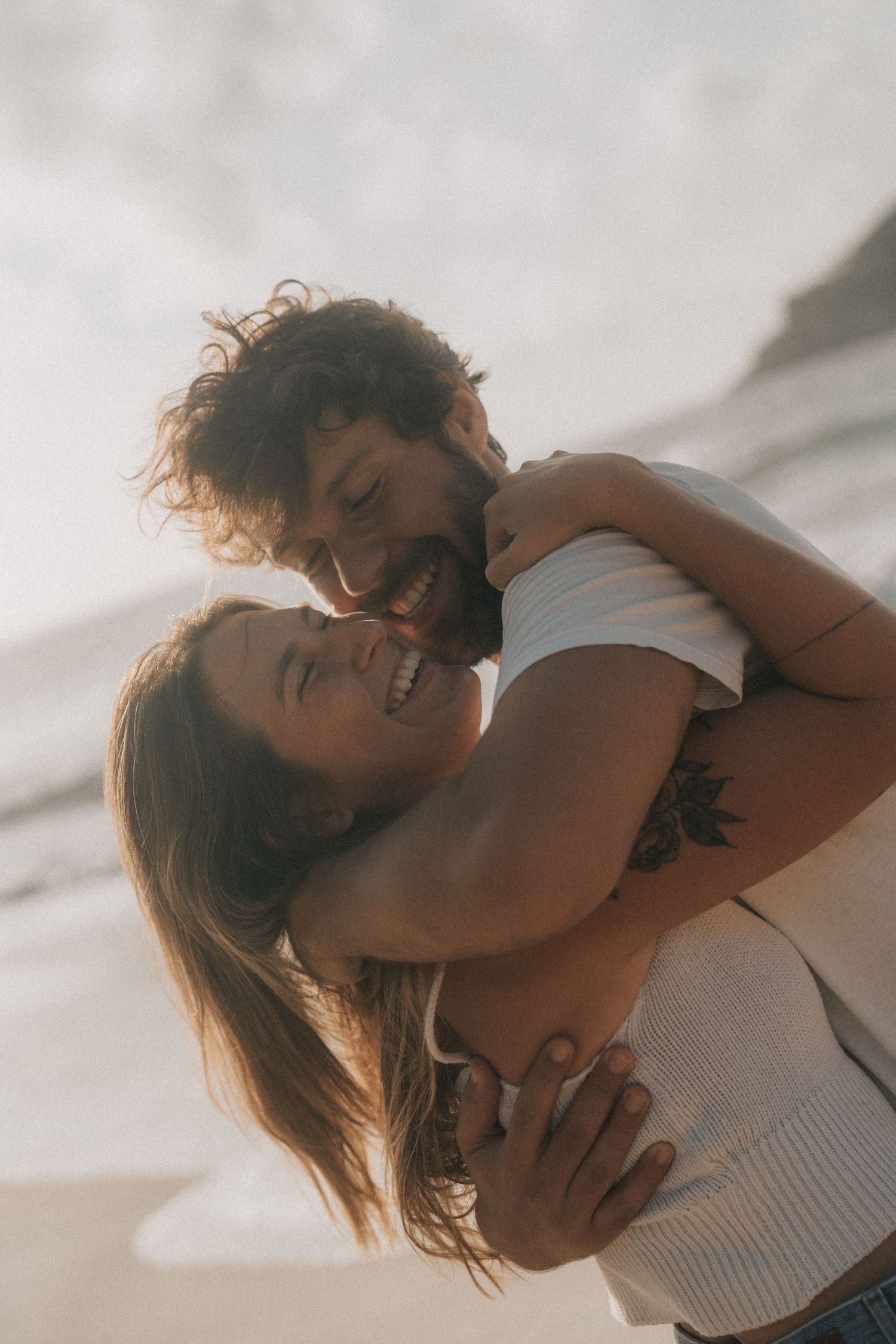 A couple shares an intimate embrace at sunset, illuminated by golden light against a dreamy outdoor backdrop.
