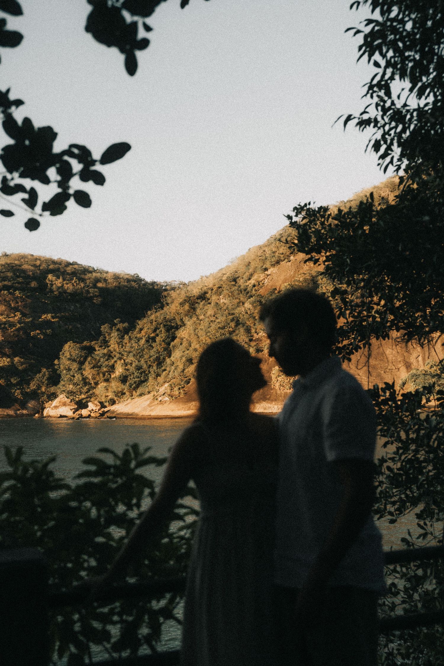Four silhouettes stand in front of a tranquil lake and mountain landscape during golden hour.