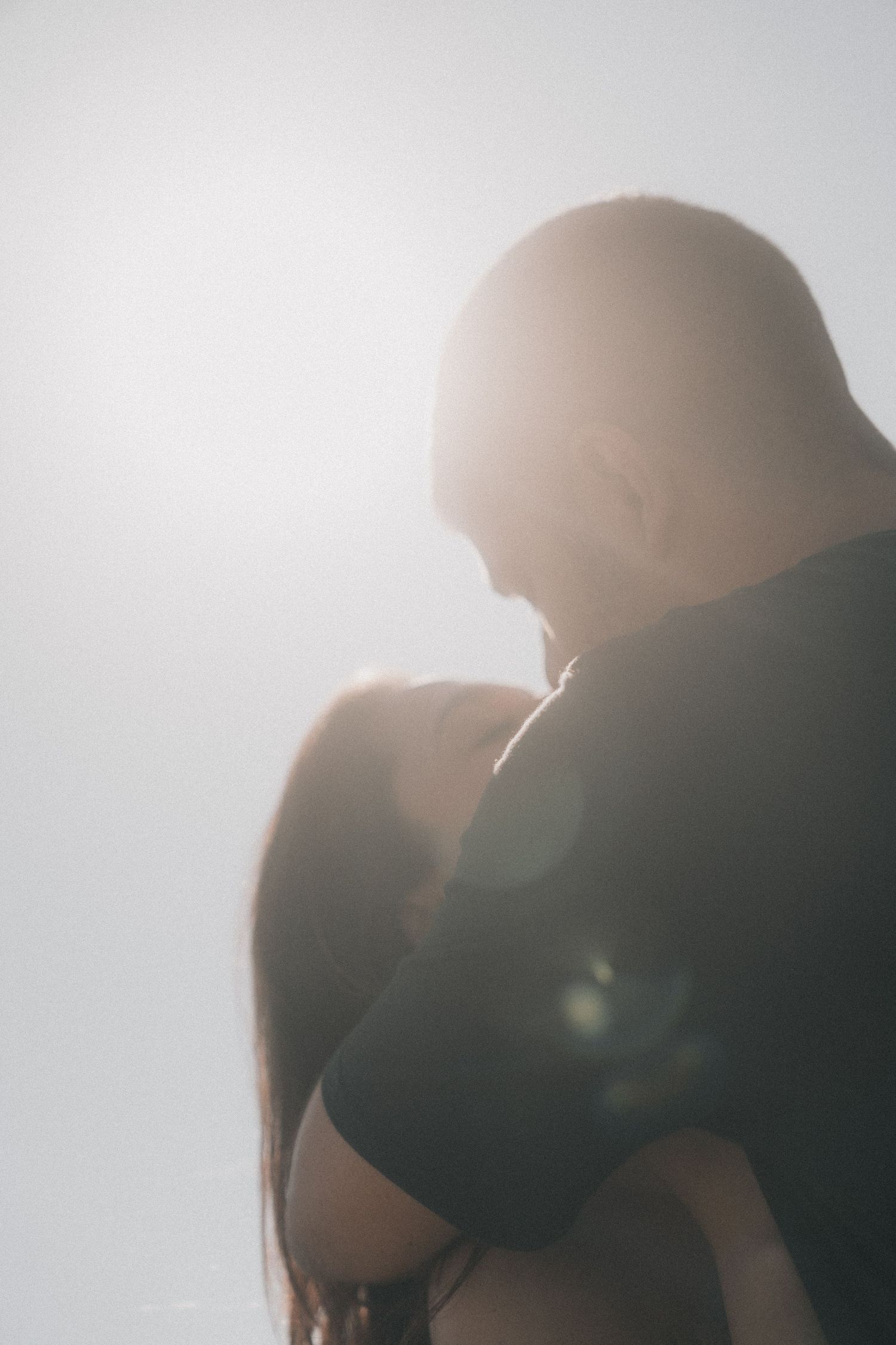 A silhouetted couple stands together in soft sunlight creating a dreamy, romantic backlit scene.