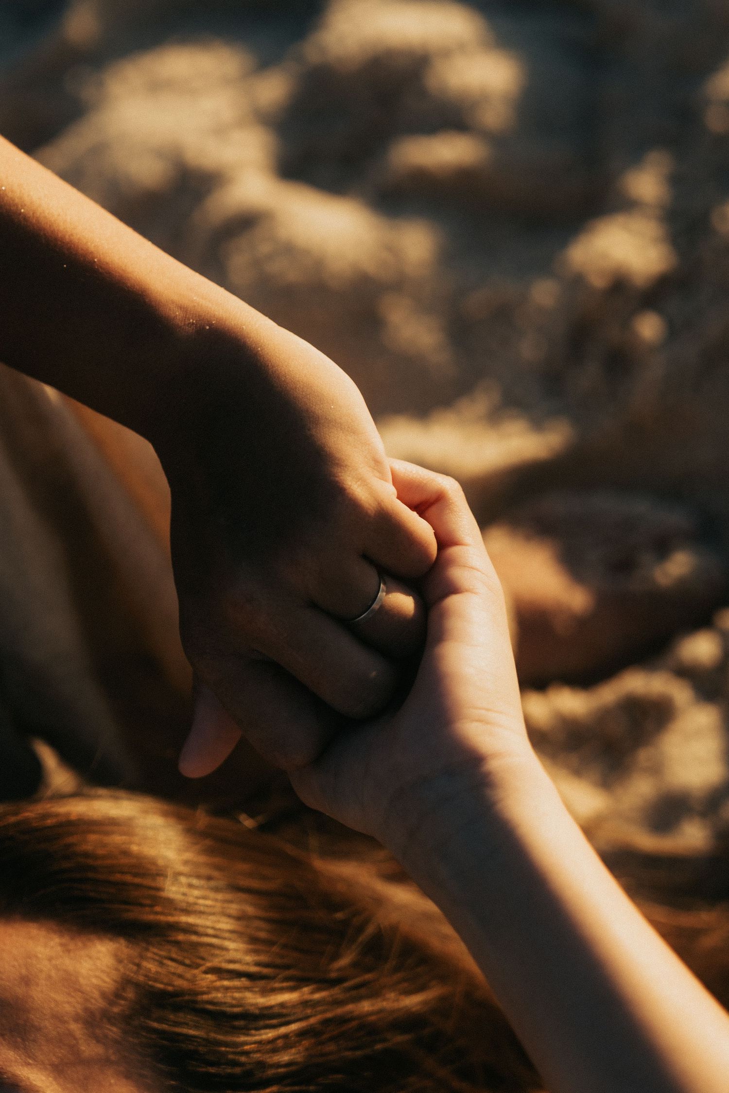 Close-up view of two hands gently reaching toward each other against a dark textured background in warm lighting.