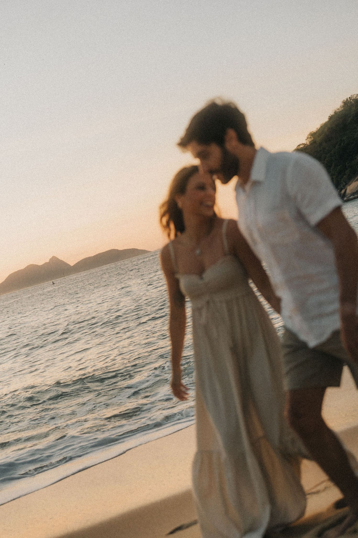 Two silhouettes dance together on a romantic beach at sunset with waves rolling in the background.
