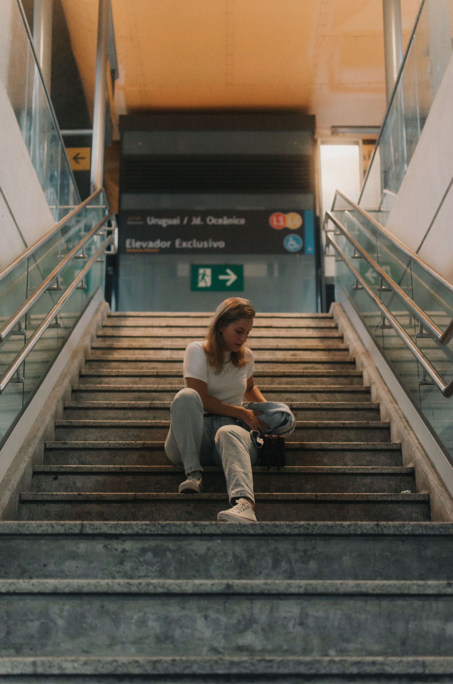 Someone sits alone at the bottom of concrete stairs in a building, creating a moody and solitary atmosphere.