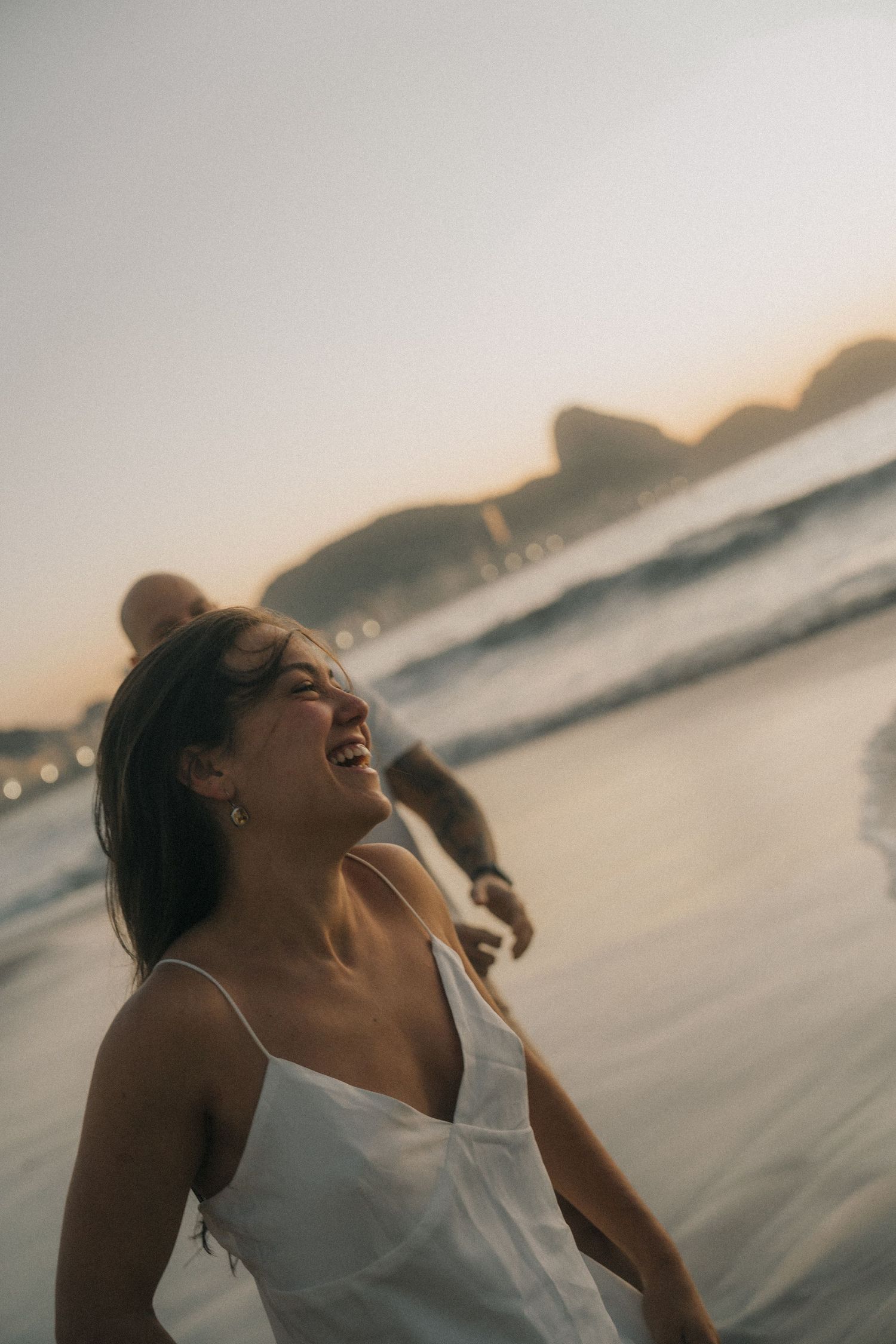 Four progressive images show a person in a white top enjoying a carefree moment at sunset by the ocean.