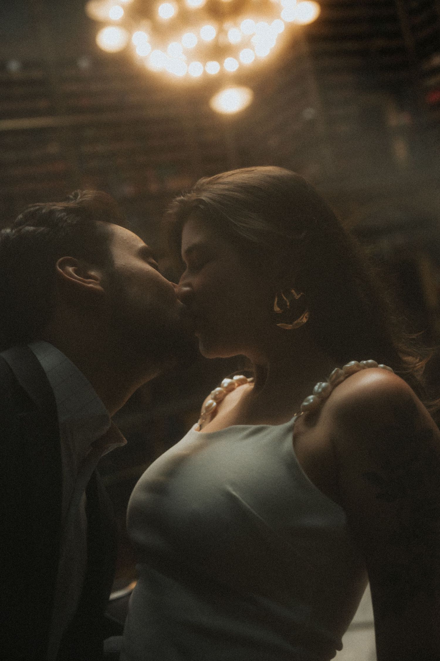A romantic silhouette of a couple sharing an intimate moment under warm glowing lights at a wedding reception.