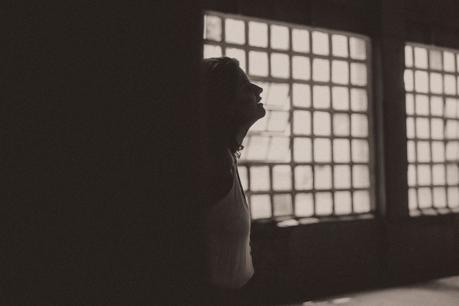 Natural window light creates dramatic shadows on figure silhouettes against a minimalist interior with gridded windows.