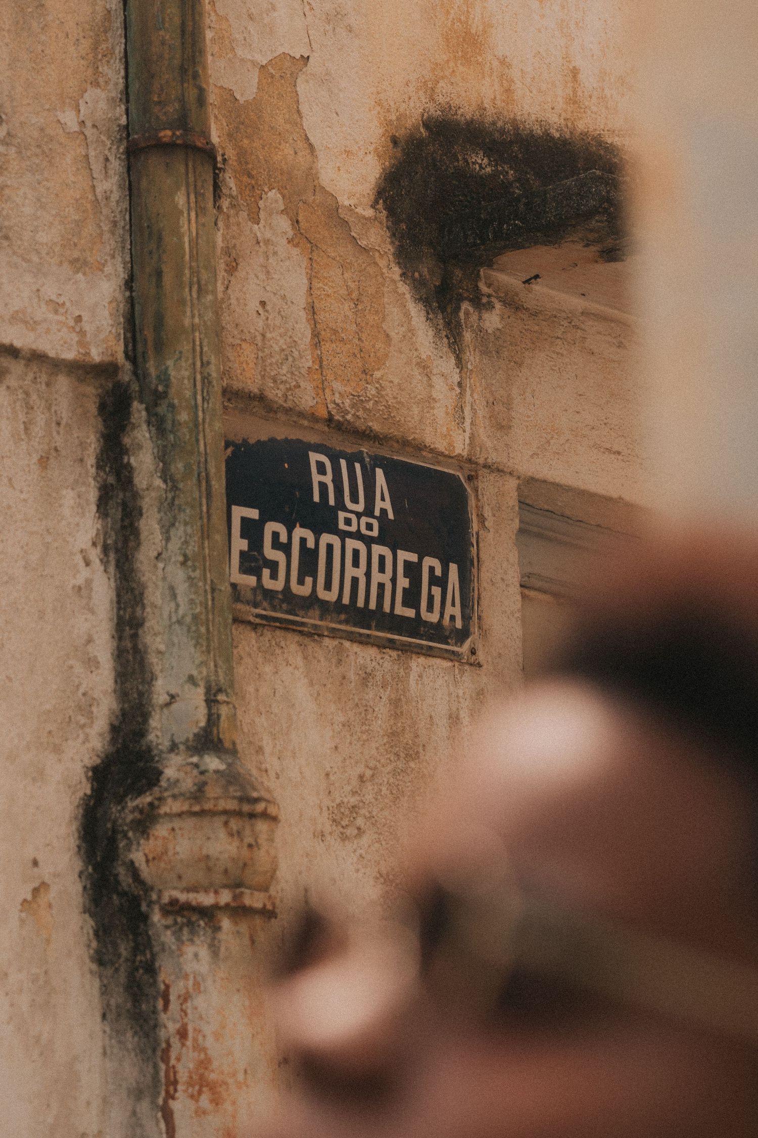 Street sign showing 'RUA ESCARREGA' mounted on weathered beige wall with faded lettering.