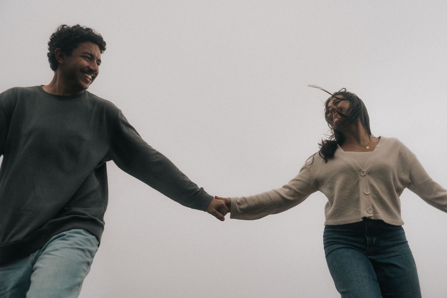 Person in black sweater and jeans dancing energetically against a white background.